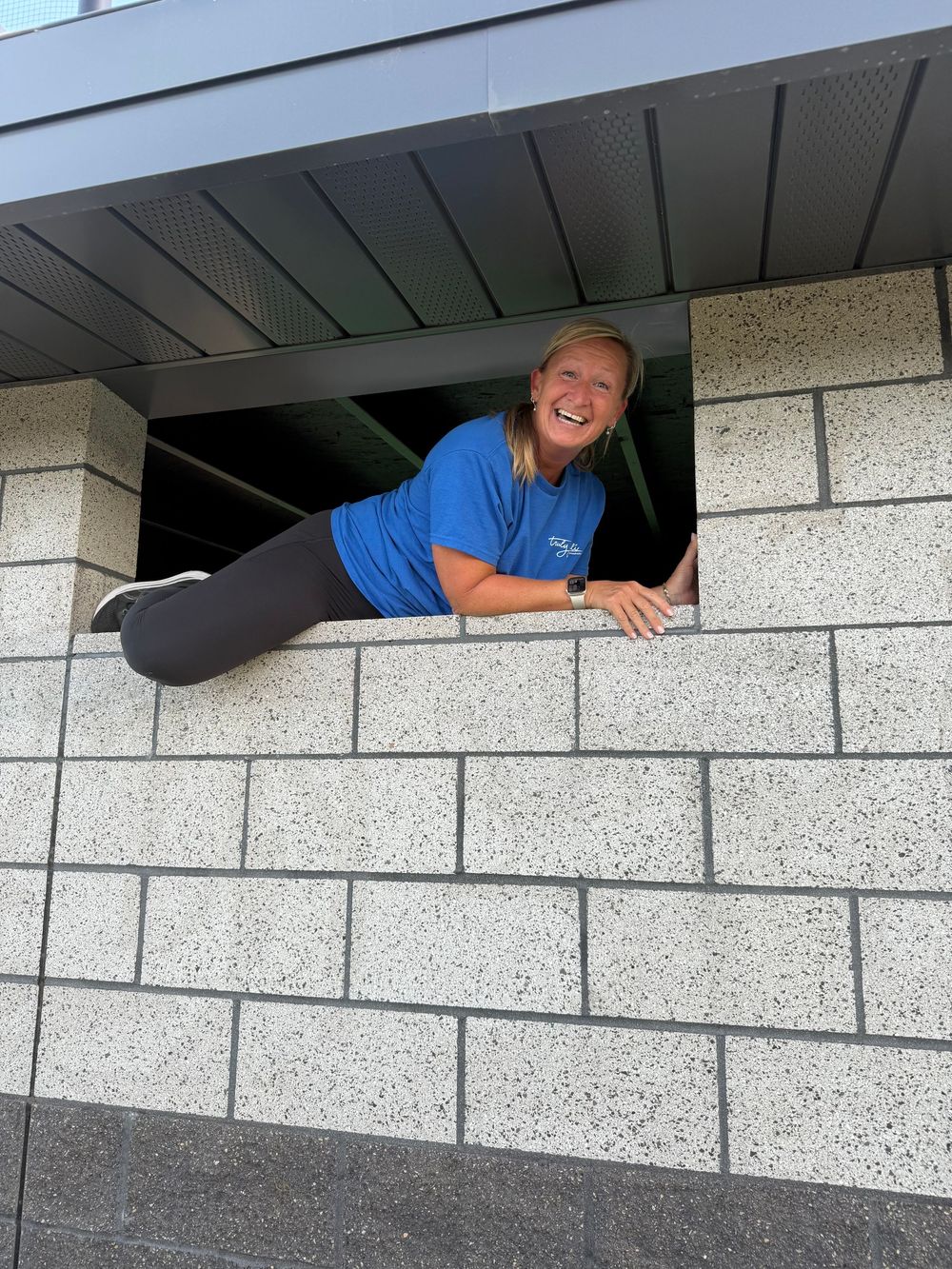 A photo showing someone playfully peeking through a small window opening in a baseball dug out.