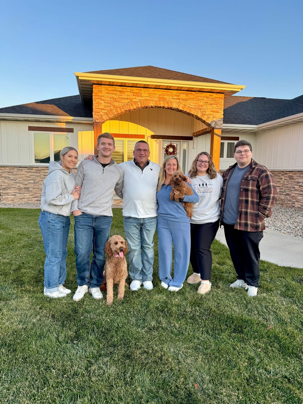 A family photo with their two dogs standing on a lawn in front of a house exterior with stone accents.
