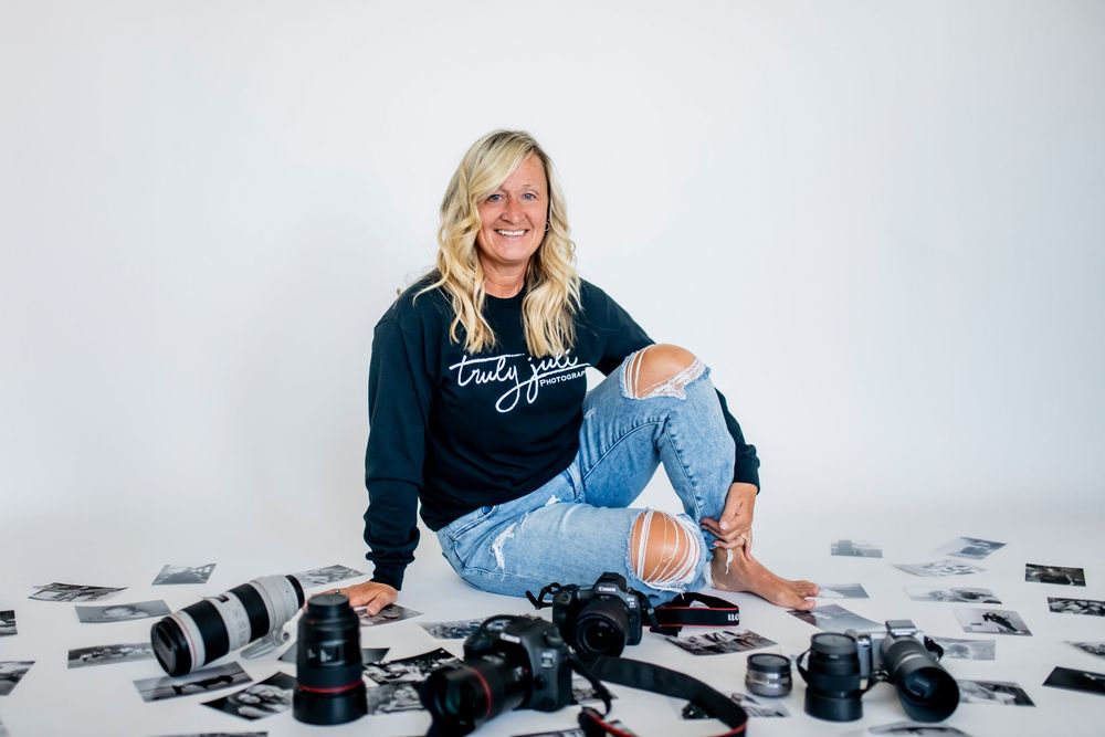 Professional photographer surrounded by camera equipment and black and white photo prints on white background.