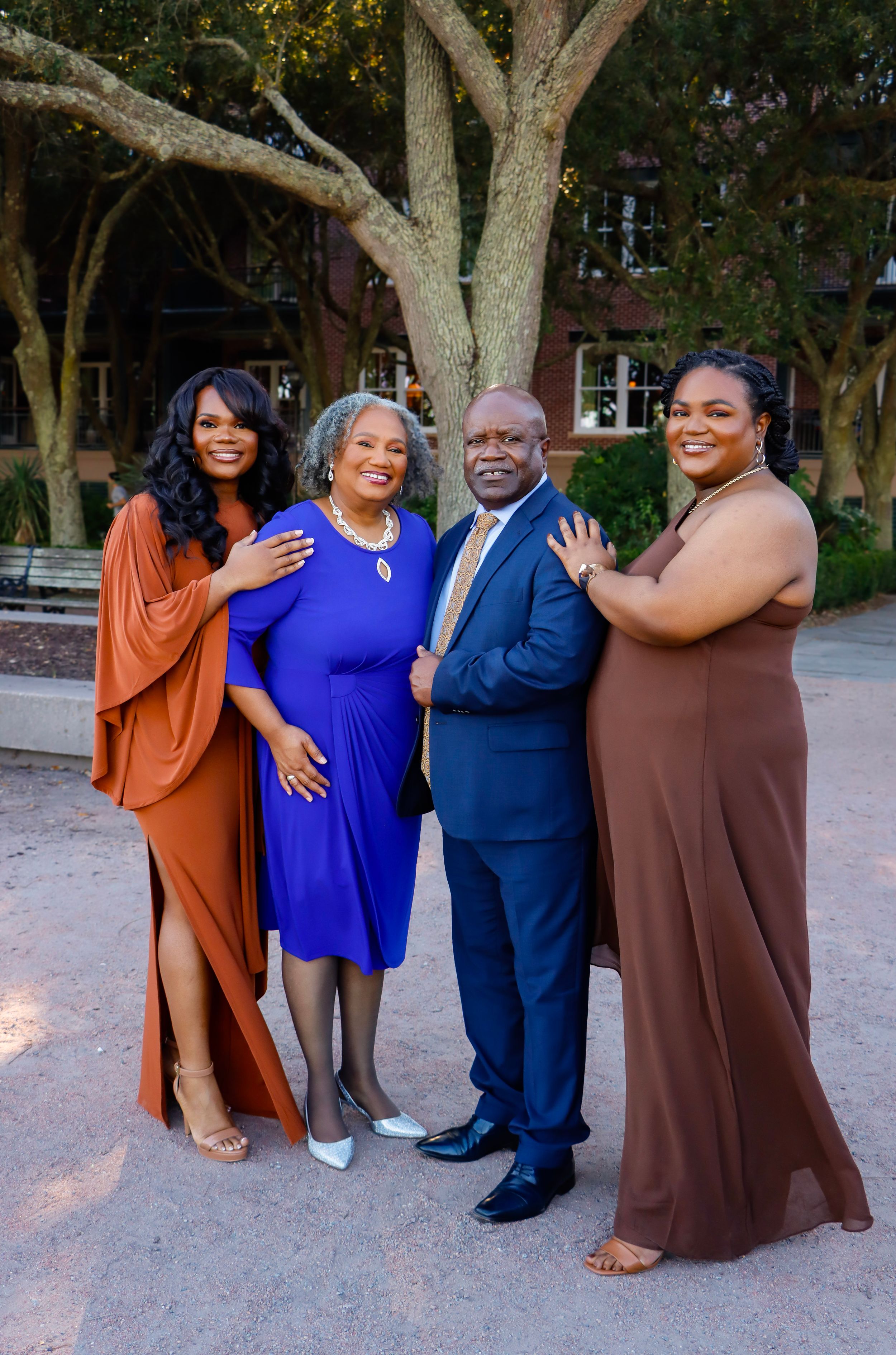 Family of four posing outdoors at dusk in Downtown Charleston, wearing coordinated blue, rust, and brown formal attire.