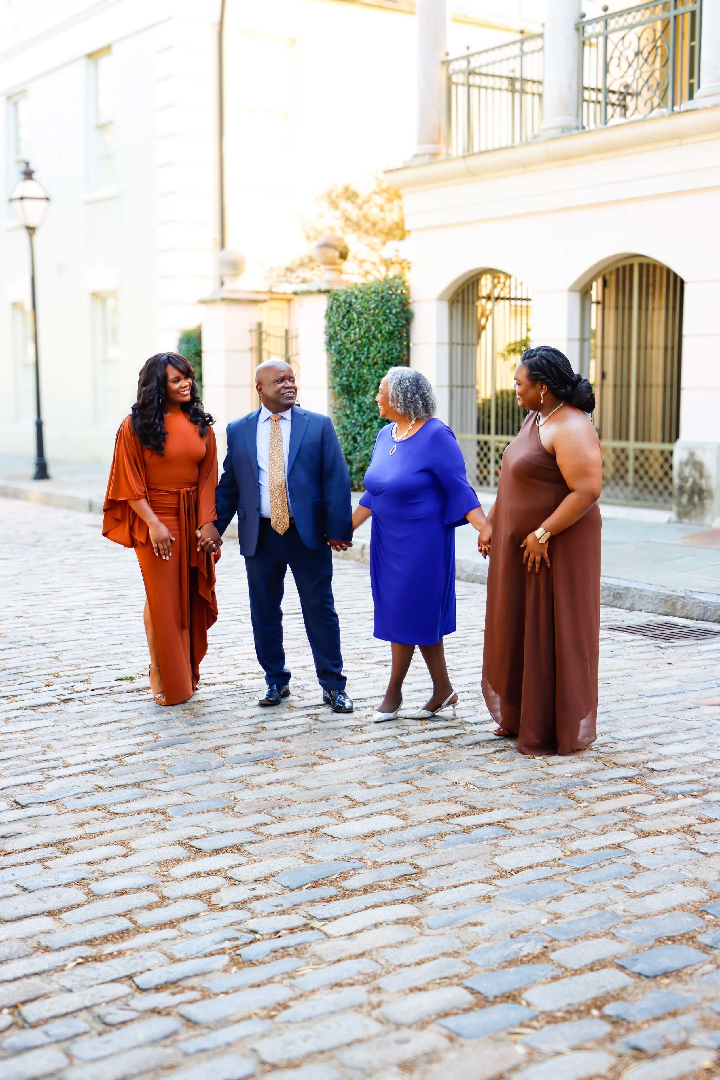 Family of four walking together on cobblestone street in elegant rust, blue, and brown formal outfits.