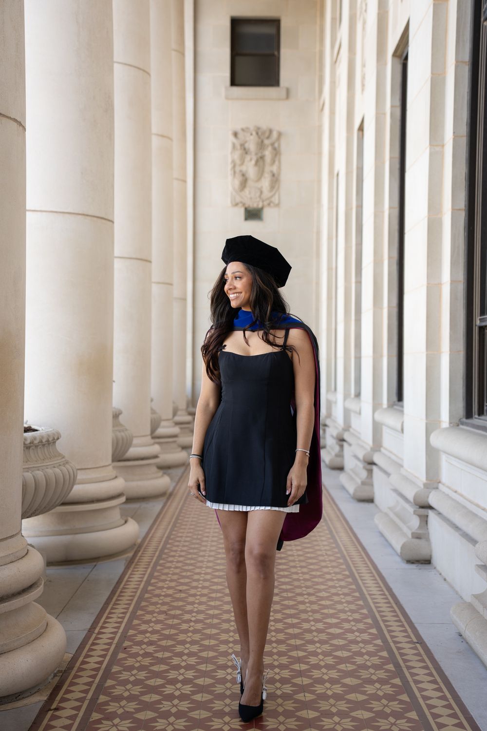 A graduate in a black dress posing between the classical white columns of the Jack K. Williams building at Texas A&M.