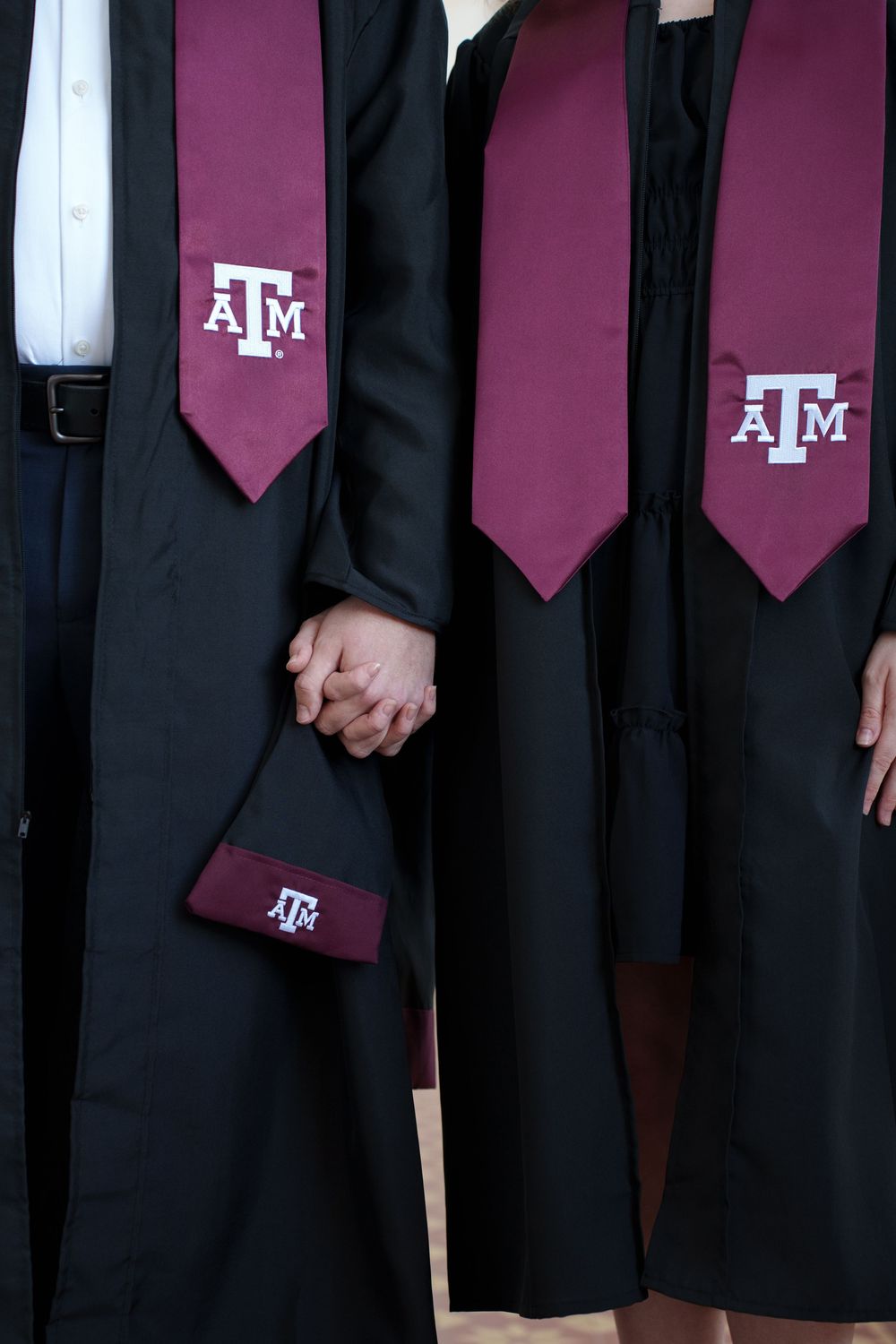 The image shows several people wearing black graduation gowns with maroon ties or sashes, representing graduates of Texas A&M University.
