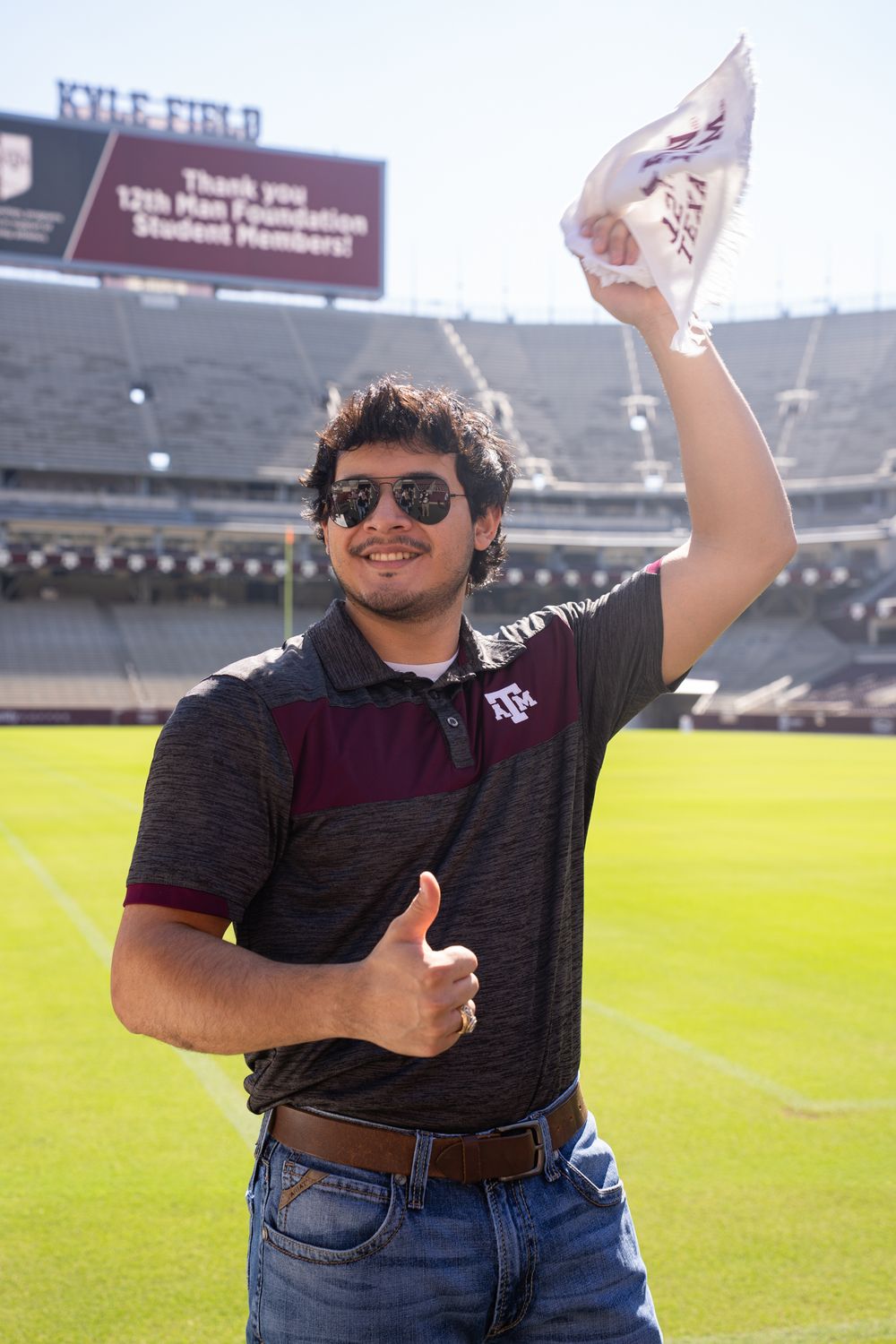 Texas A&M graduate in a maroon top and jeans posing in front of Kyle Field in College Station.