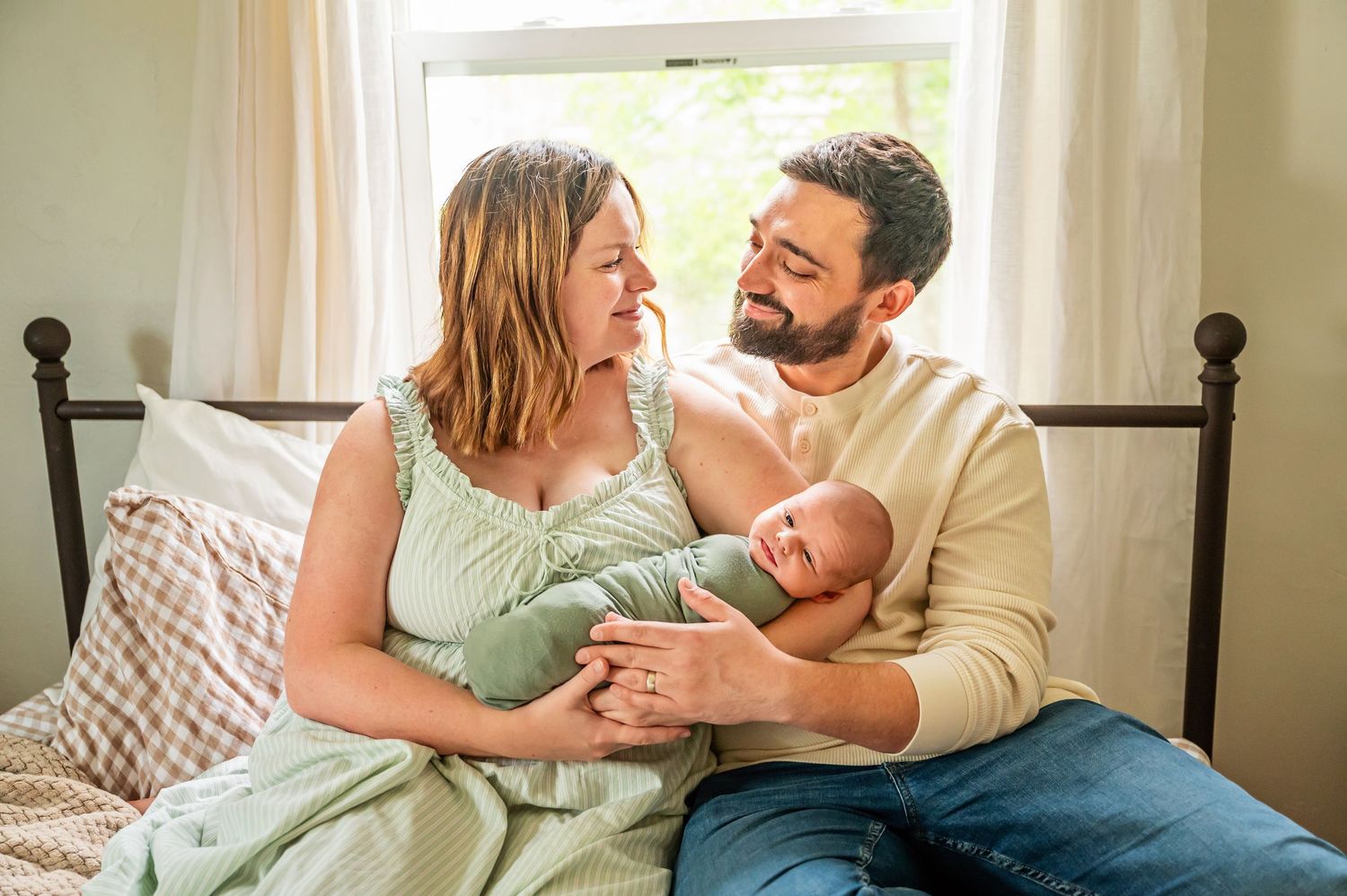 A newborn in burgundy wrap is tenderly held while sleeping.