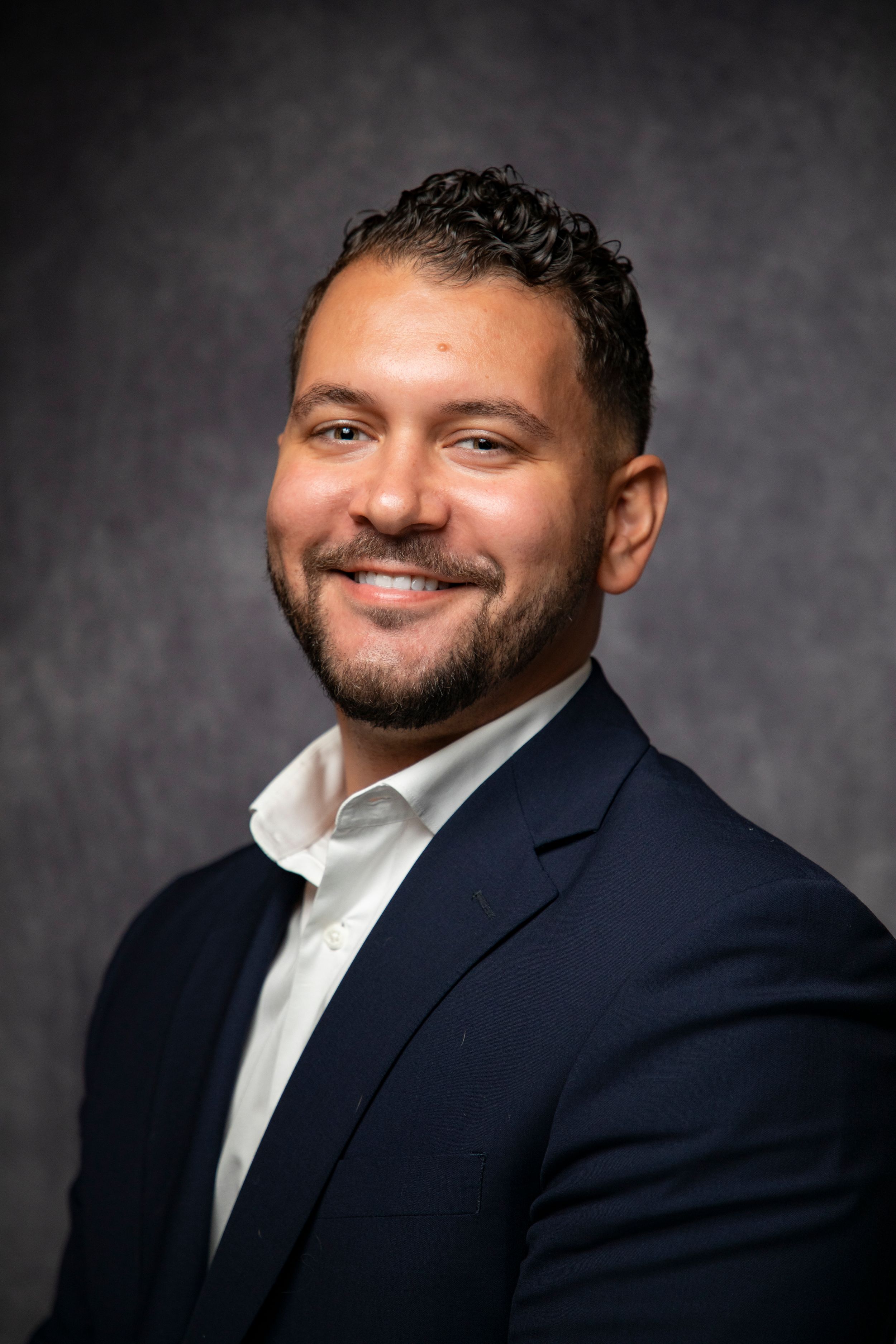 Professional headshot series of person in navy suit and white shirt against dark background.