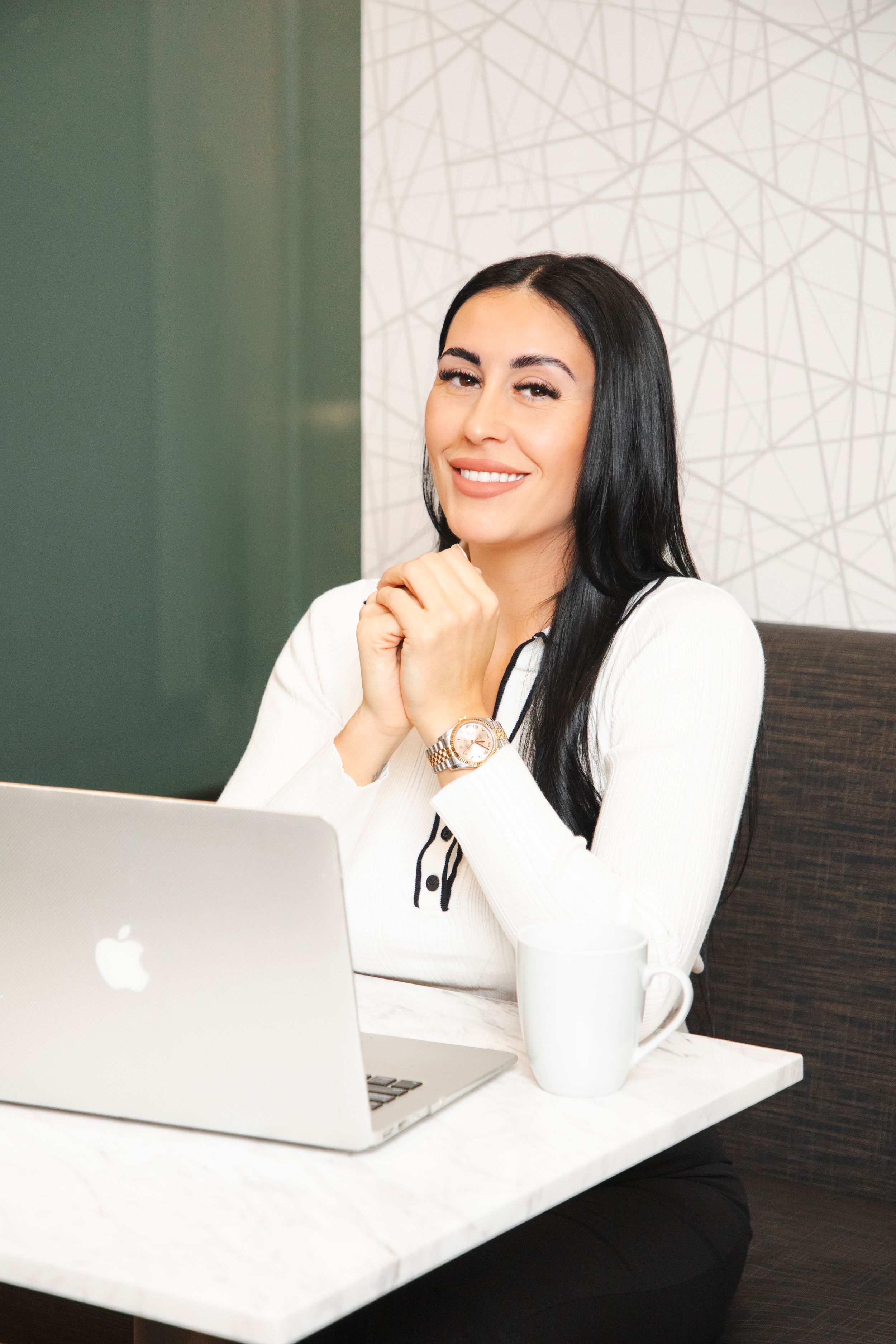 Professional woman in white sweater working on laptop in modern office setting.
