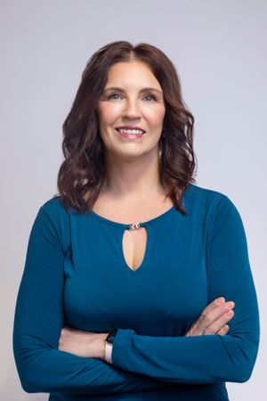 Woman in long-sleeve blue top posing confidently against neutral backdrop.