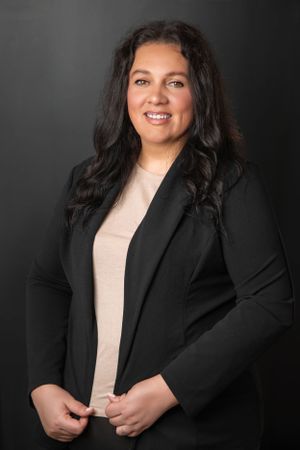 Studio portraits in professional black blazer and light top against dark background.