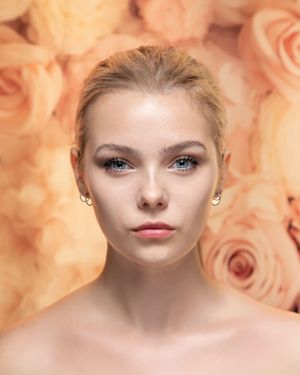 Artistic beauty portrait with soft peach-toned floral background and dramatic lighting.