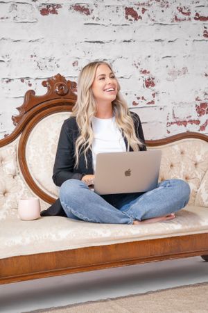 Person working on laptop while sitting on vintage sofa against distressed brick wall.