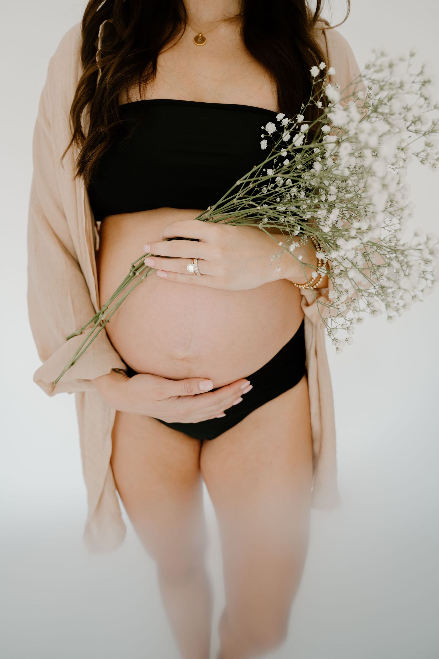 Black and white maternity photo of pregnant woman in lingerie and open white shirt cradling her baby bump.