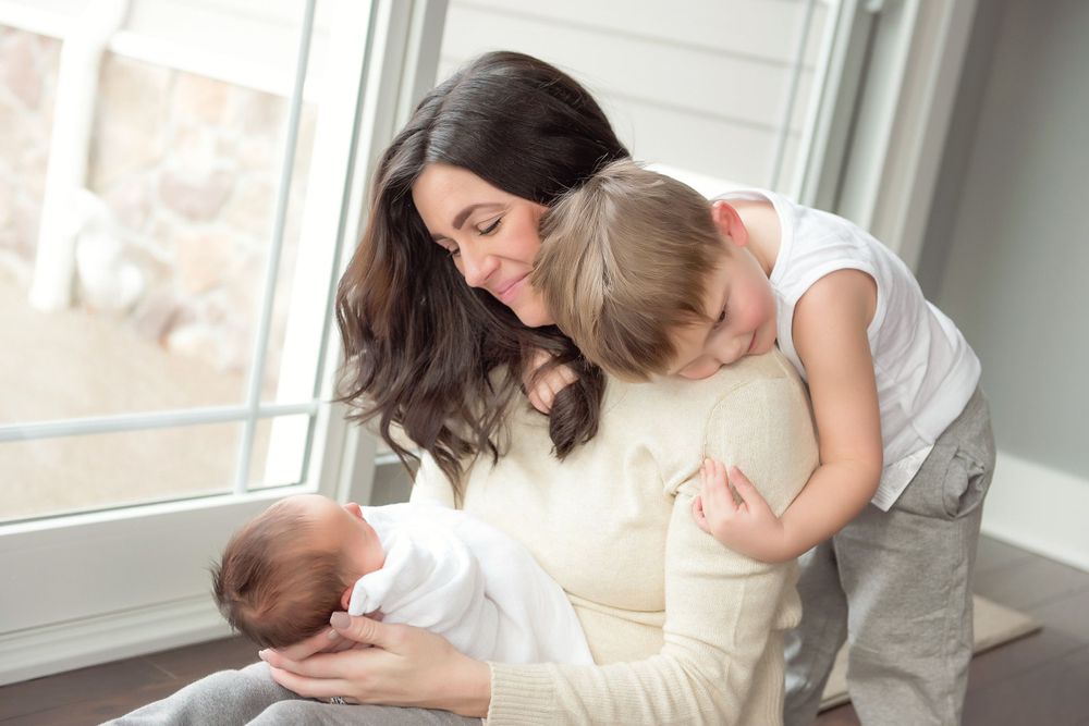 Tender family moment as parent holds newborn while sibling watches.