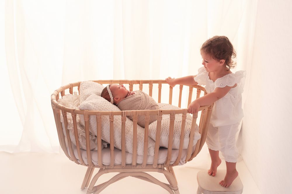 Toddler looking at newborn sister in bassinet backlit photo