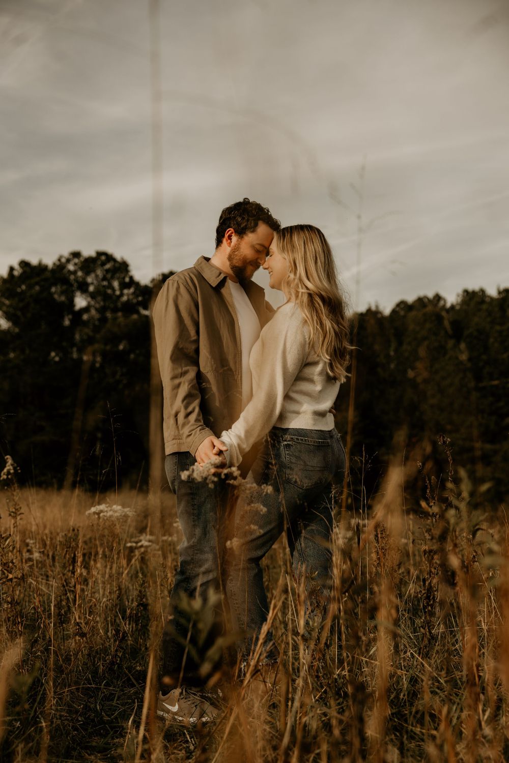 Romantic couple in casual wear share an intimate moment standing in a golden field at sunset.