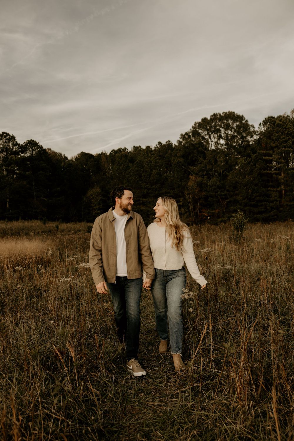 Couple walking together through a golden autumn field at sunset wearing casual attire.
