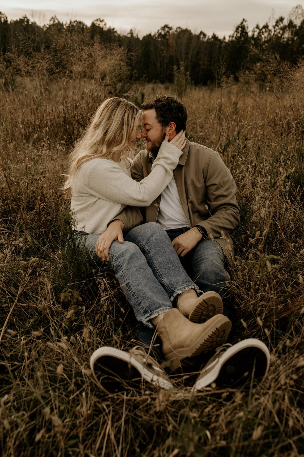 A romantic couple shares an intimate moment sitting in tall grass at sunset in an autumn field.