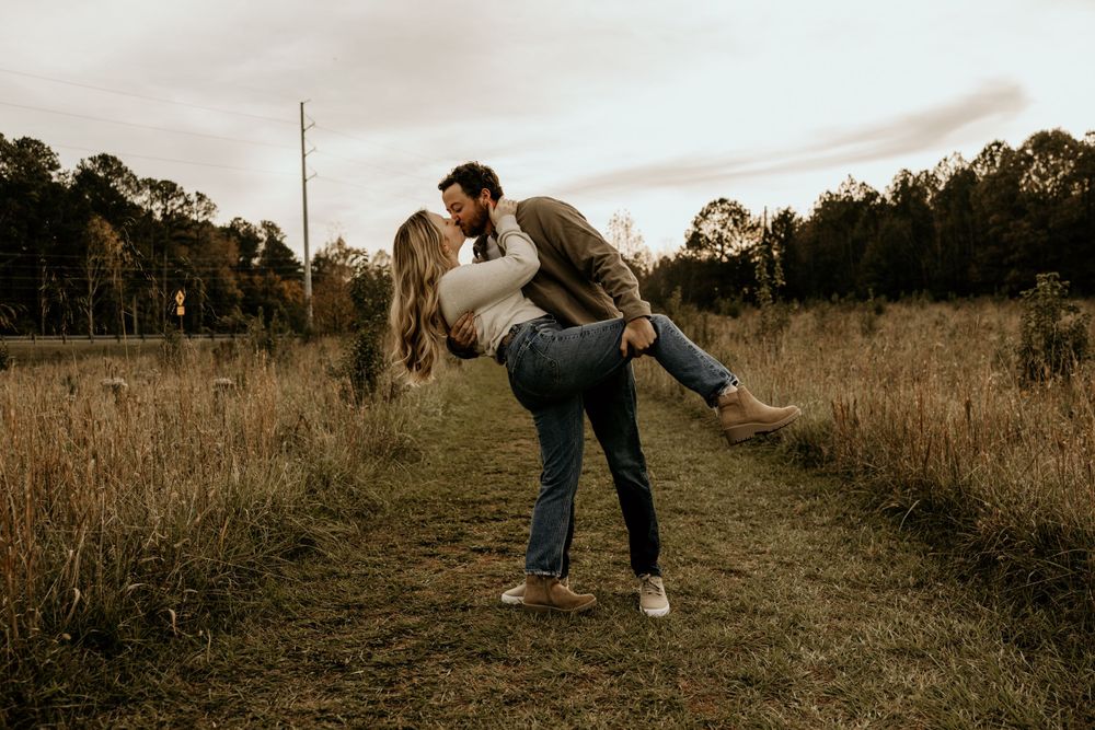 A couple shares a romantic dip pose together on a dirt path surrounded by tall grass at golden hour.