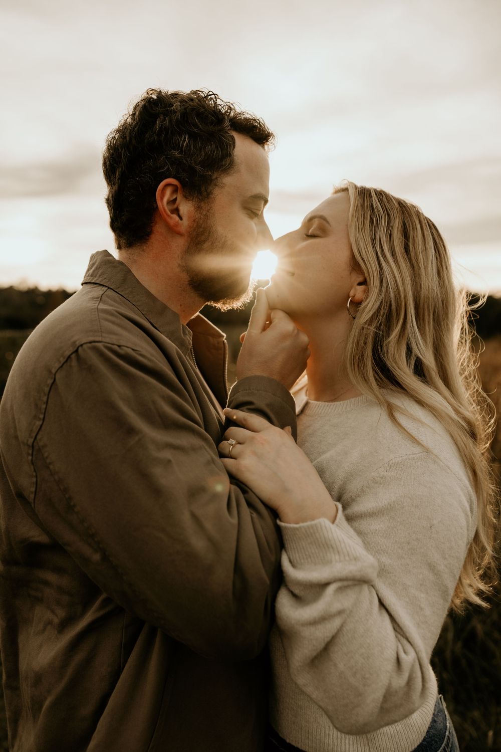 Romantic couple embracing in warm sunlight with lens flare between them in a fall field setting.