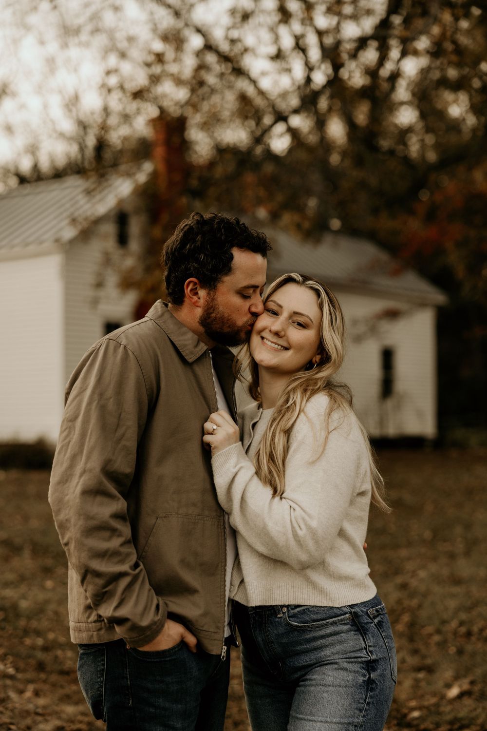 Intimate autumn portrait in front of white building with couple in casual sweaters.