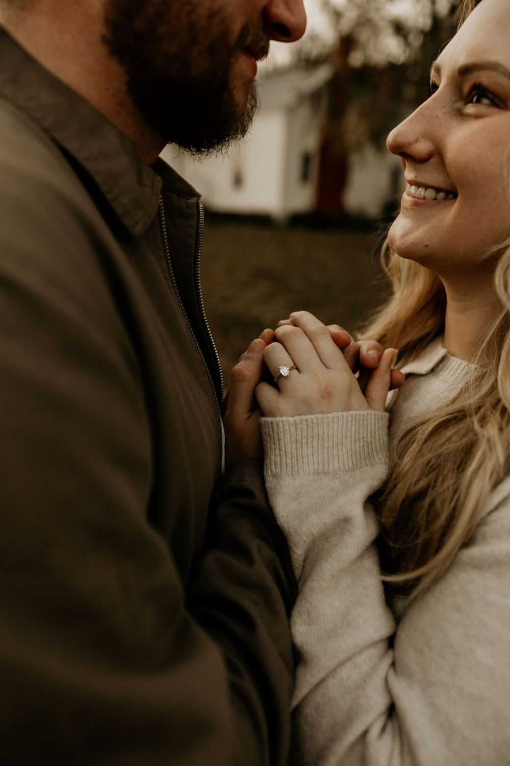 A couple shares an intimate moment outdoors while holding hands, wearing cozy sweaters in warm sepia tones.