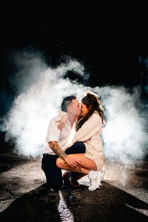 A romantic couple kisses in a dramatic cloud of white smoke against a dark background in a series of artistic photos.
