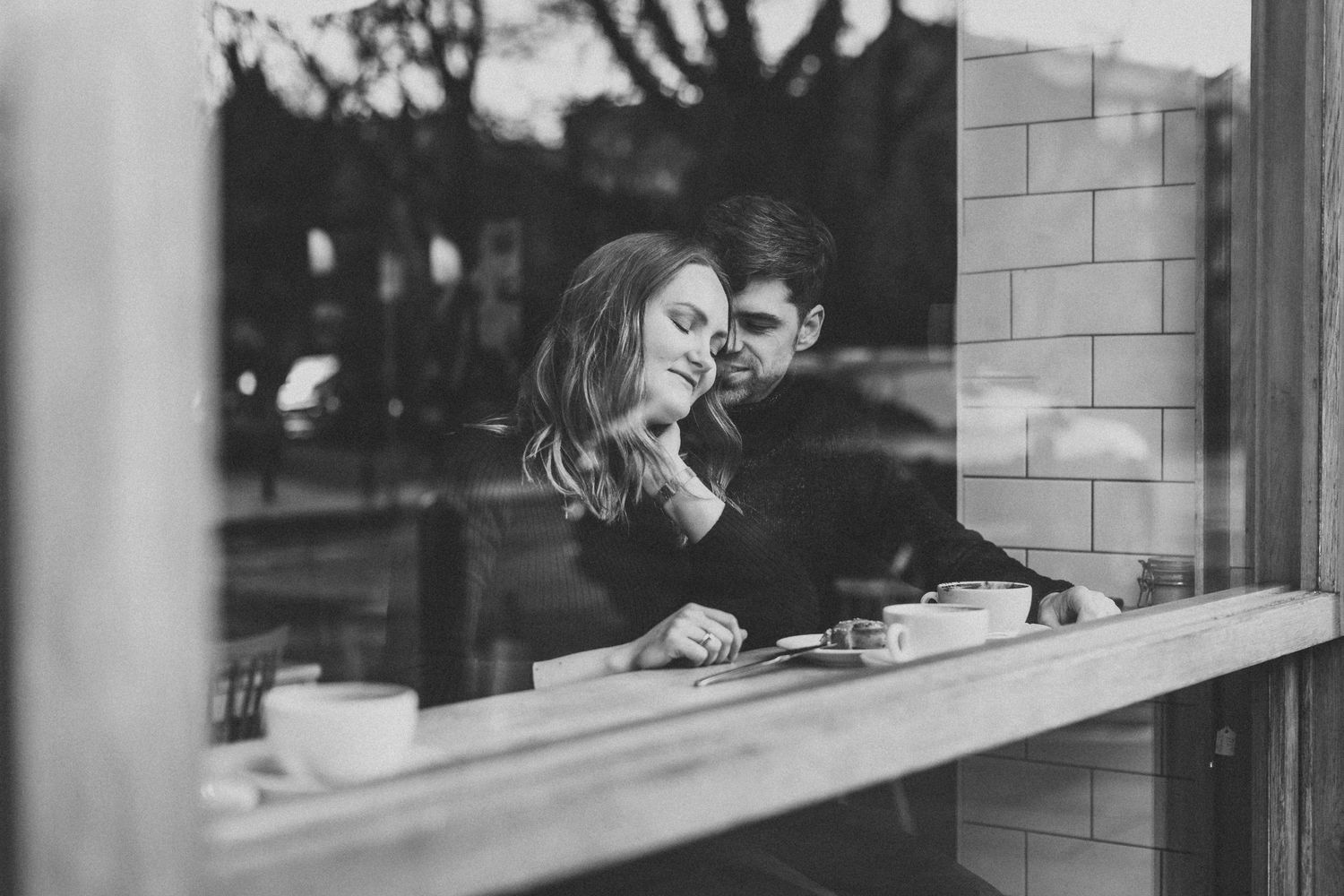 A black and white photo showing two people smiling and looking through a cafe window.