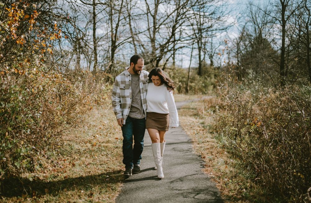 Couple walking hand in hand on a scenic path surrounded by autumn trees and shrubs on a sunny day.