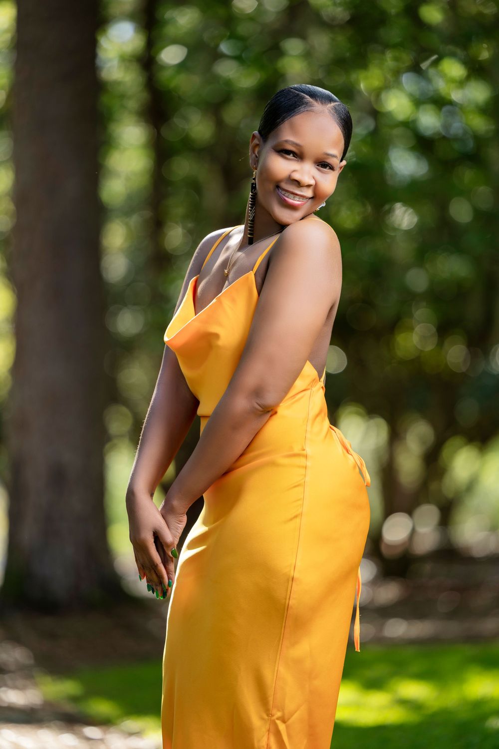 Fashion model poses in bright yellow sundress outdoors in natural garden setting.