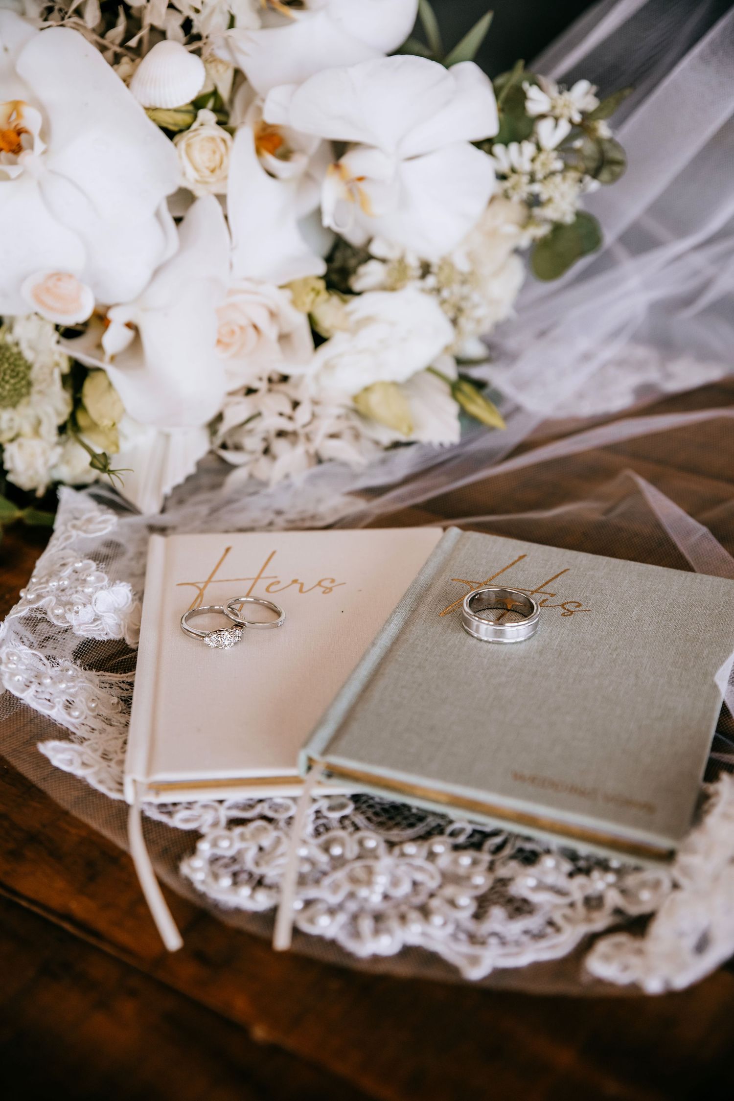 Wedding rings displayed on vow books with white orchids and roses bouquet.
