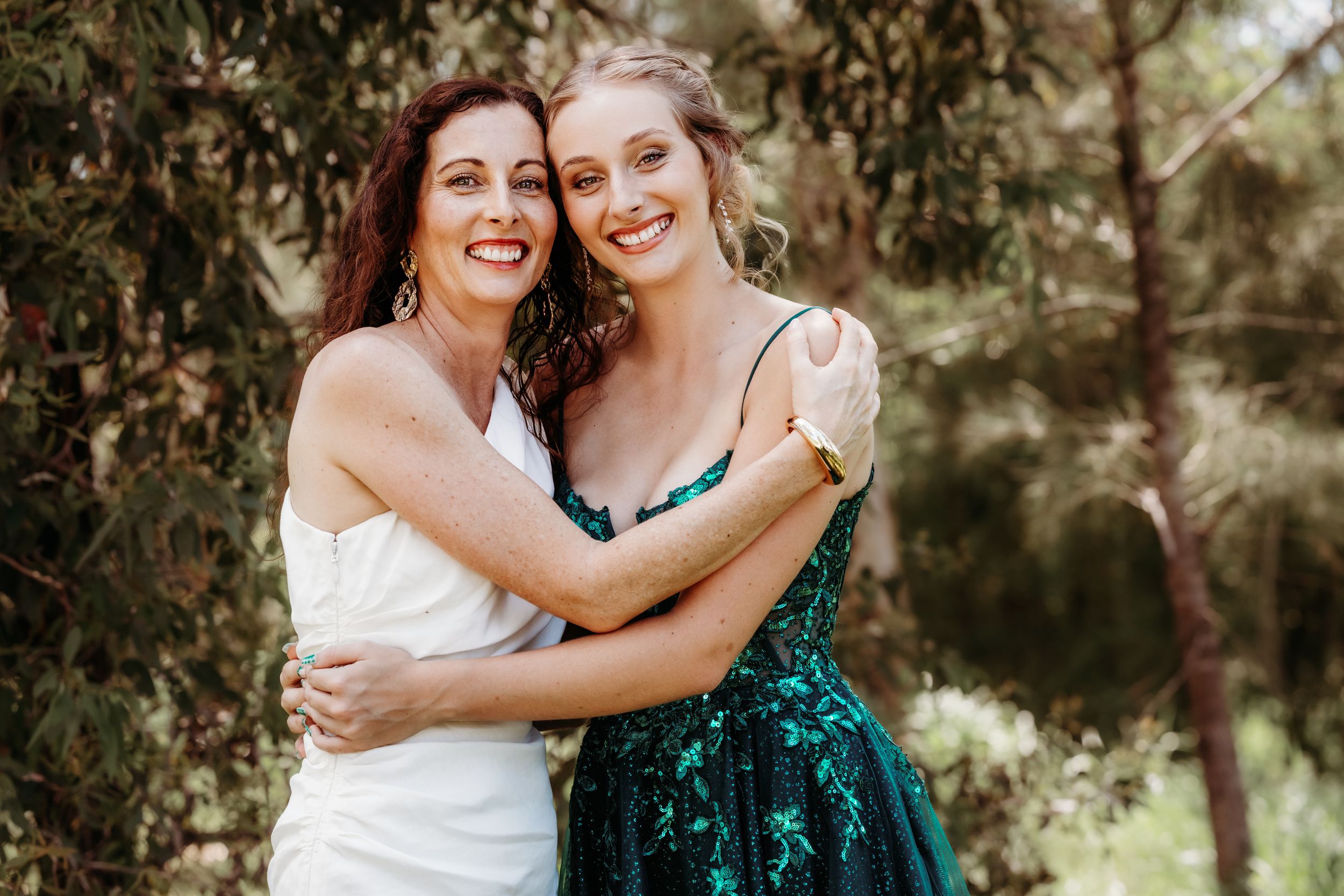 Two people embracing outdoors in a garden setting with natural sunlight filtering through trees.