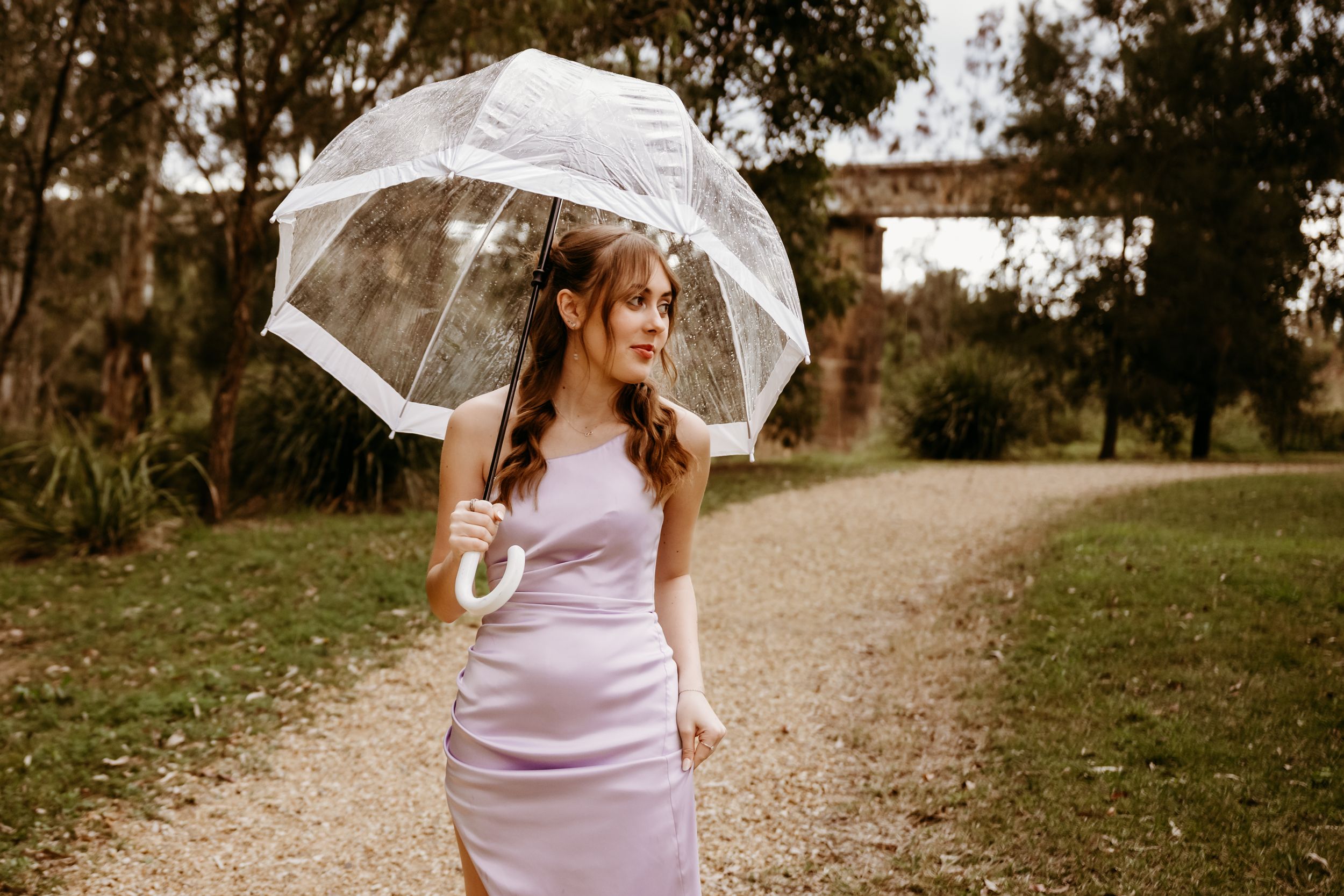 A bride in a pink dress glides along a rustic path holding a vintage white lace parasol on an autumn day.