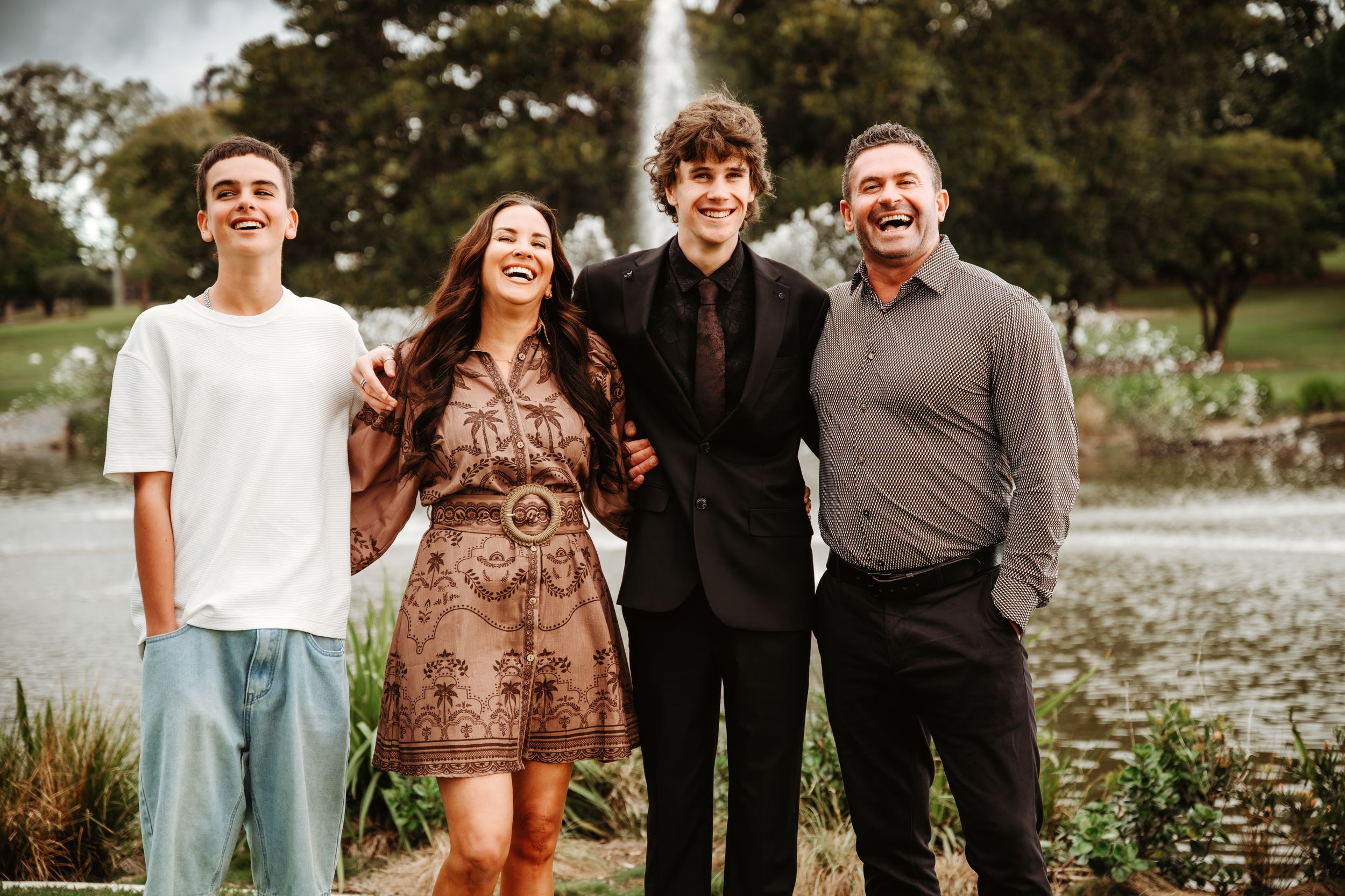 Four smiling family members pose outdoors near a fountain, dressed in casual and formal attire for a portrait.