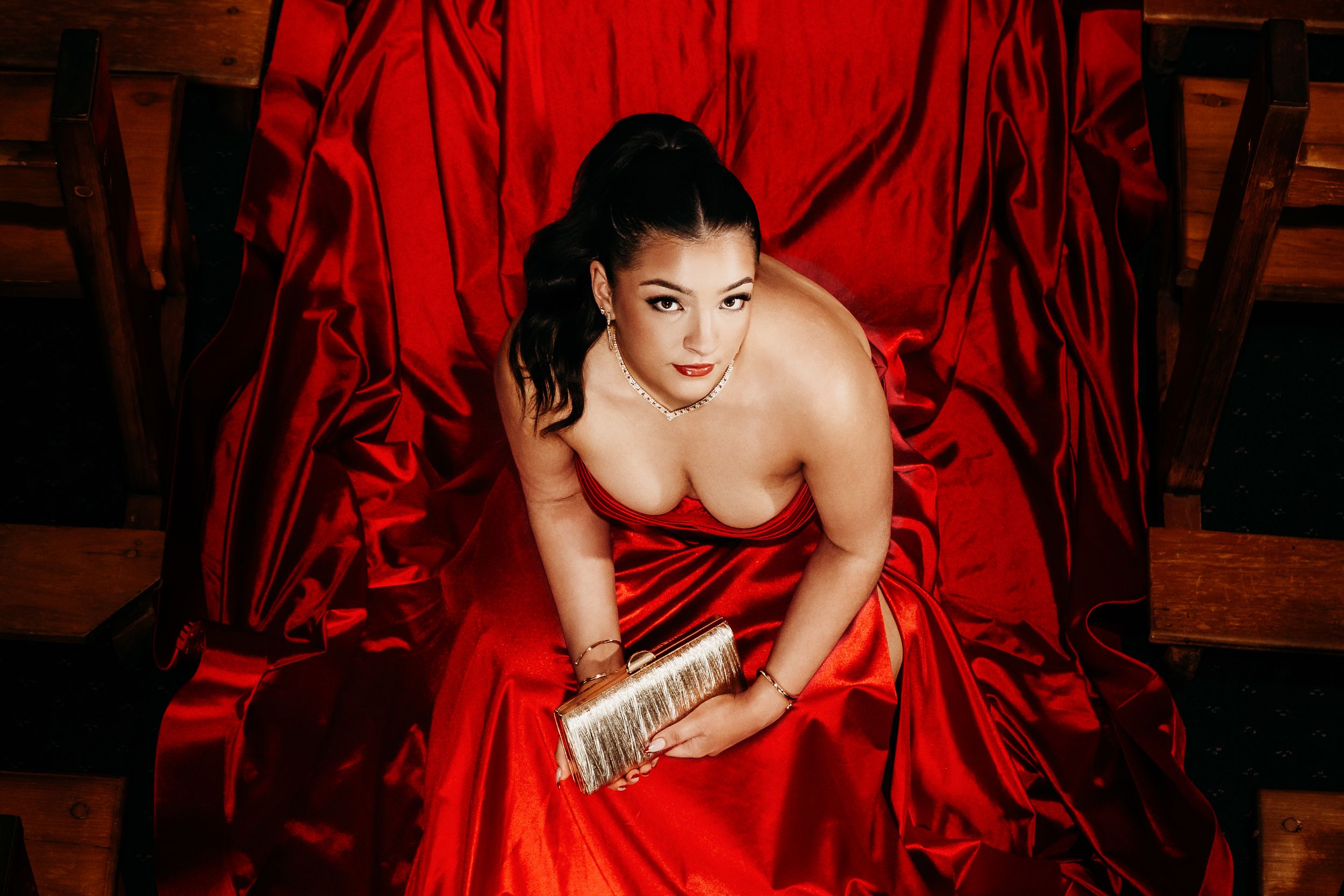 Model in flowing red dress poses dramatically against dark studio backdrop in artistic fashion series.