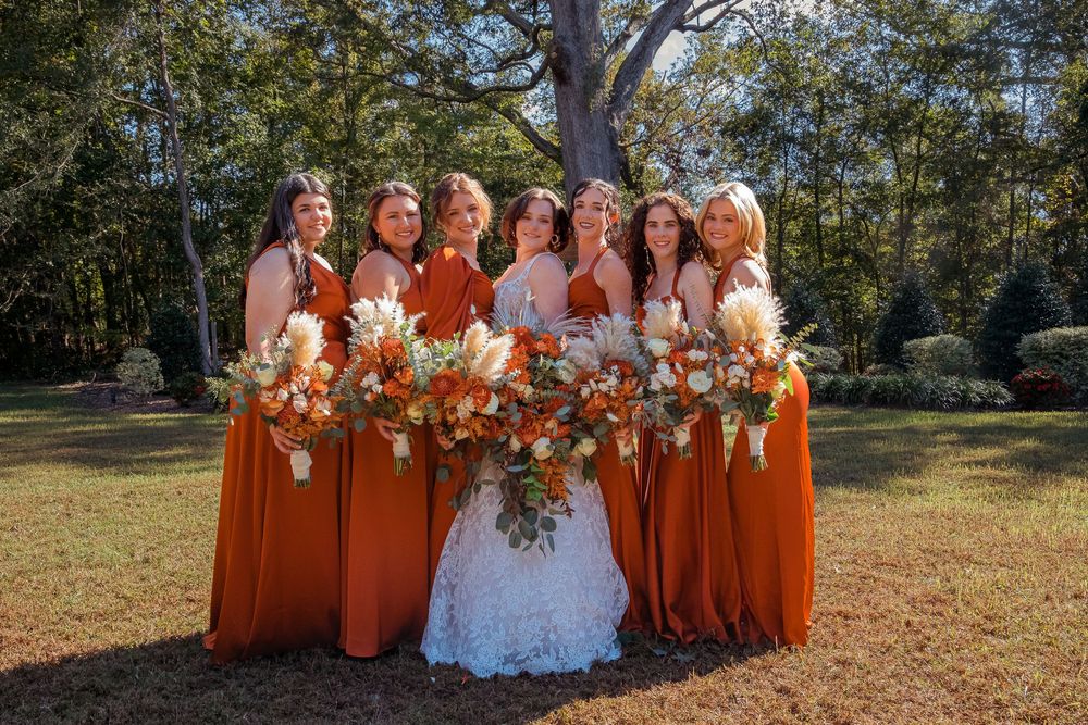 Wedding party in bright orange dresses poses outdoors on sunny autumn day.