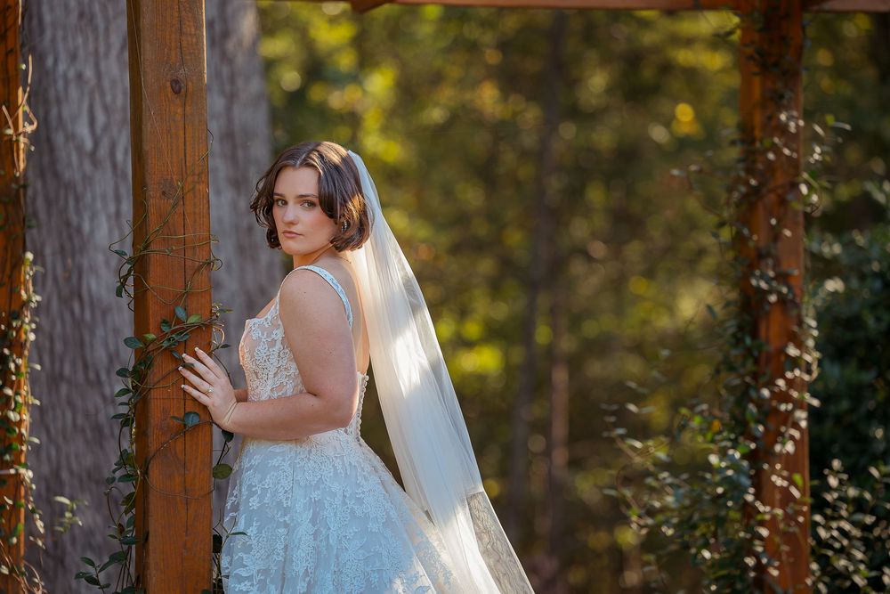 A bride in a white lace dress poses gracefully in a rustic wooden outdoor setting during golden hour.