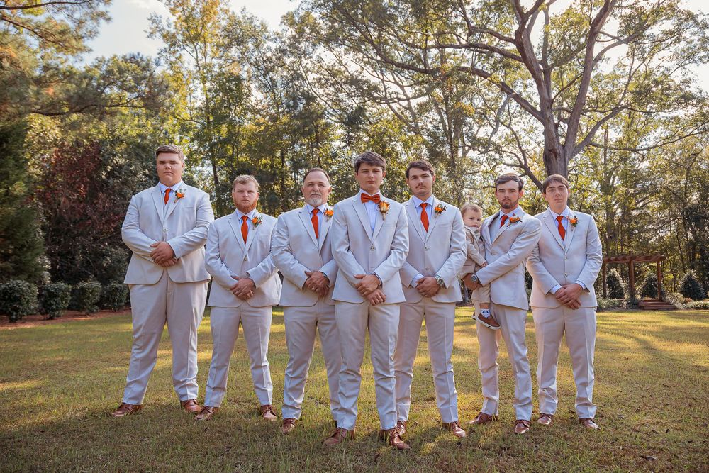 A group of people in white clothing pose together in a line outdoors during golden hour lighting.
