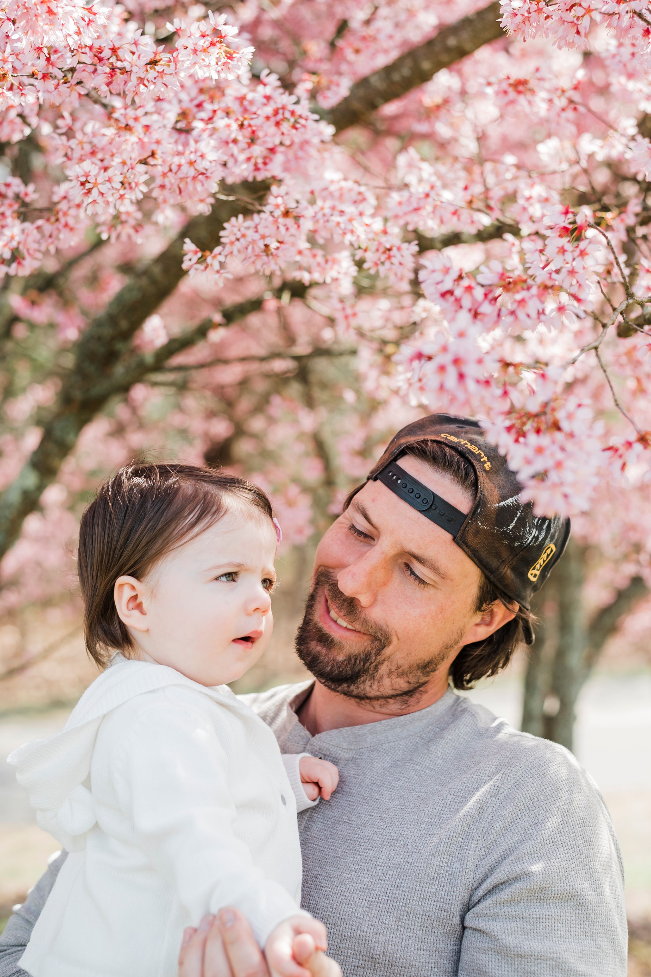Cherry blossoms frame a touching outdoor spring portrait under pink blooming trees.