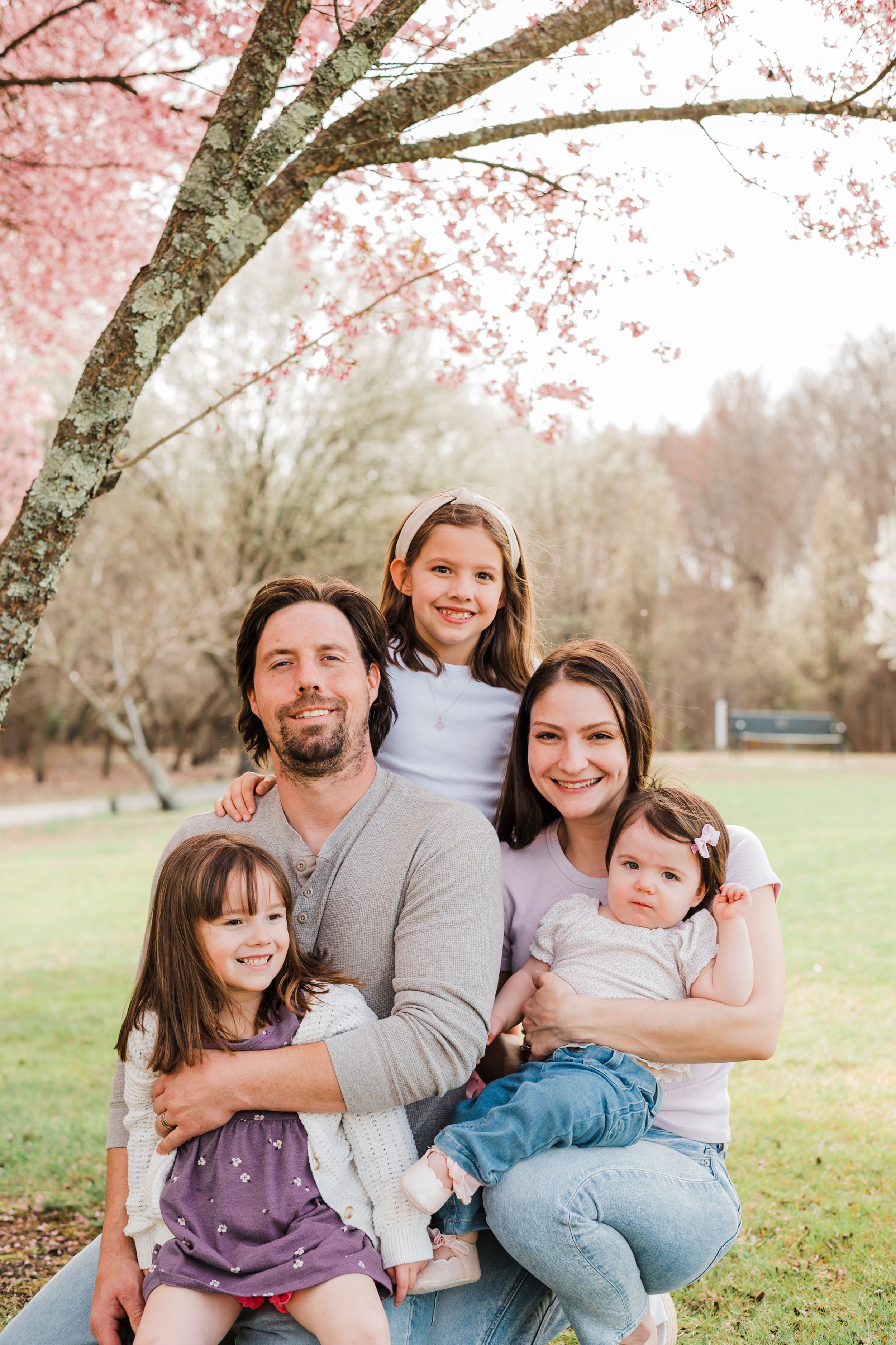 A family poses together under pink cherry blossoms in bloom during springtime.