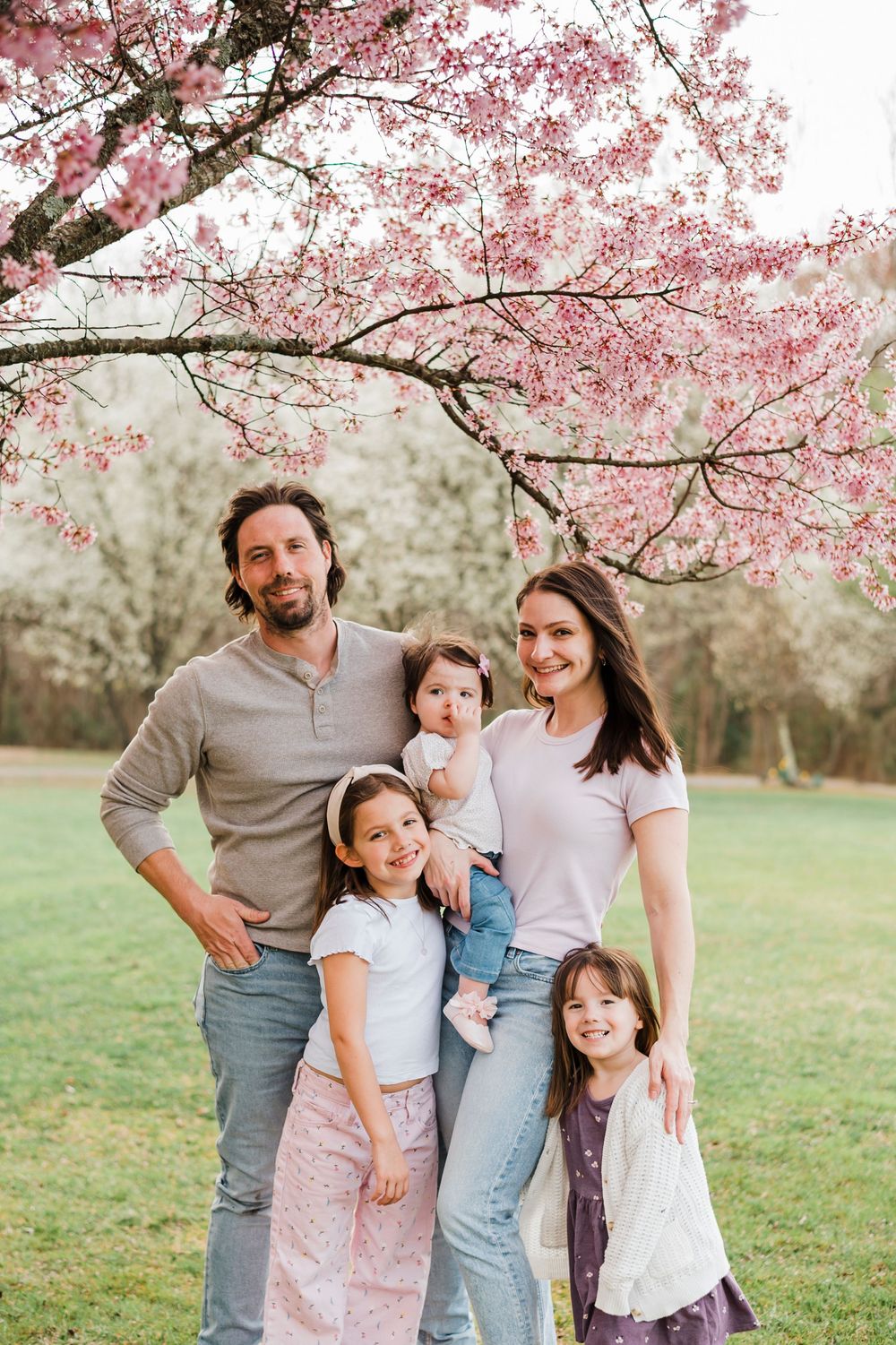 Spring family photo under blooming cherry blossom trees with pink petals.