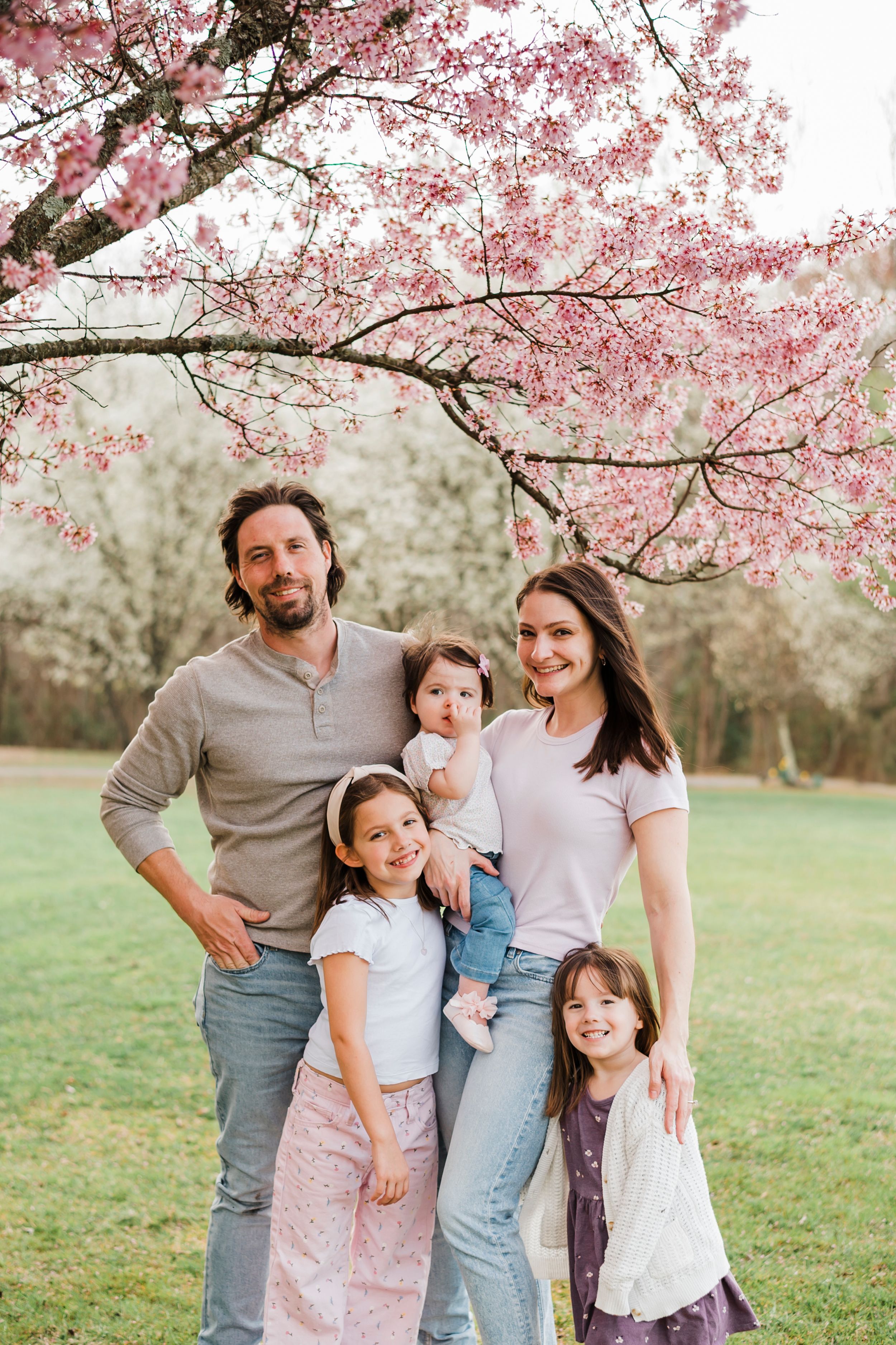 Spring family photo under blooming cherry blossom trees with pink petals.