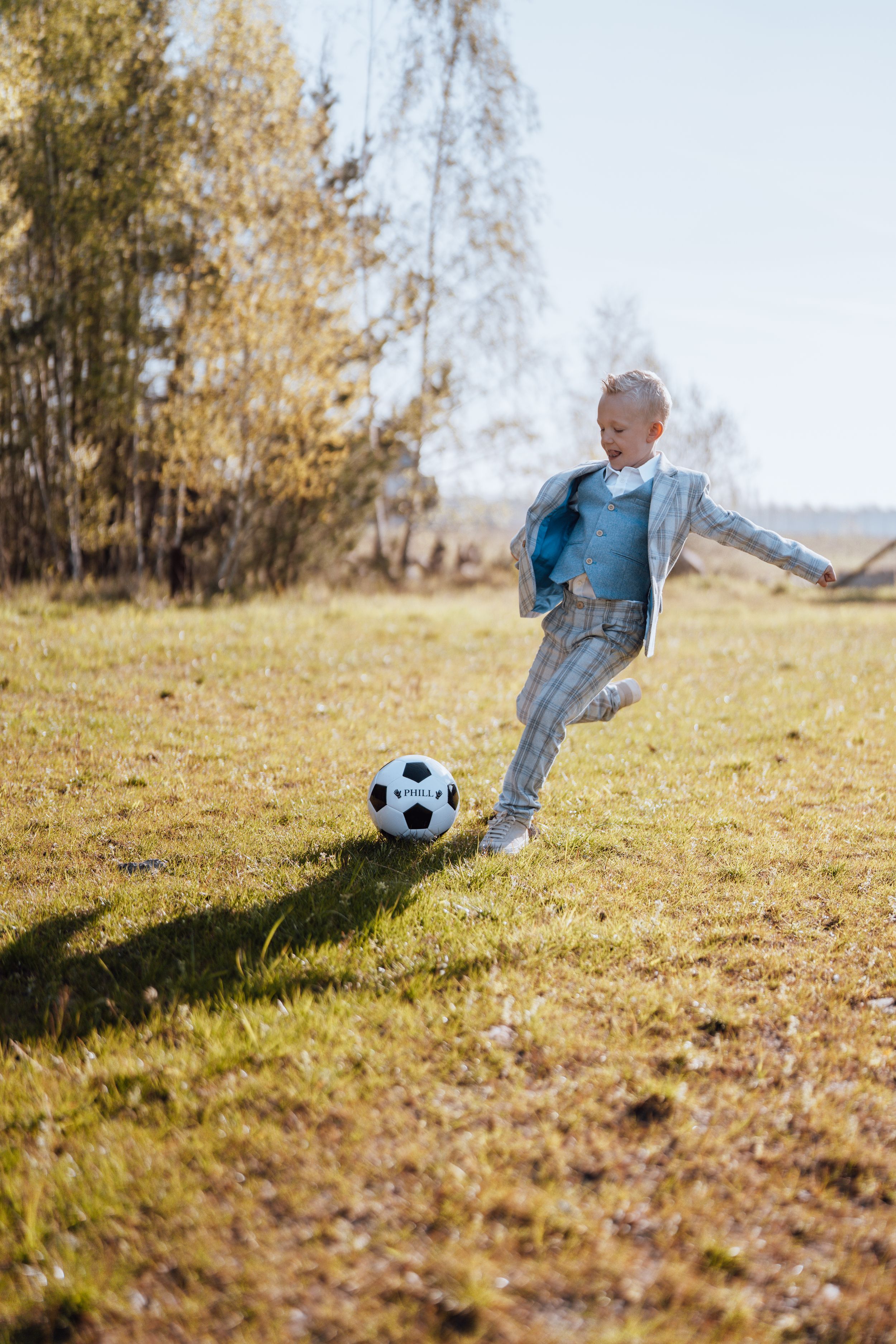 Actieve persoon die een voetbal trapt op een zonnige herfstdag in een grasveld met herfstbomen op de achtergrond.