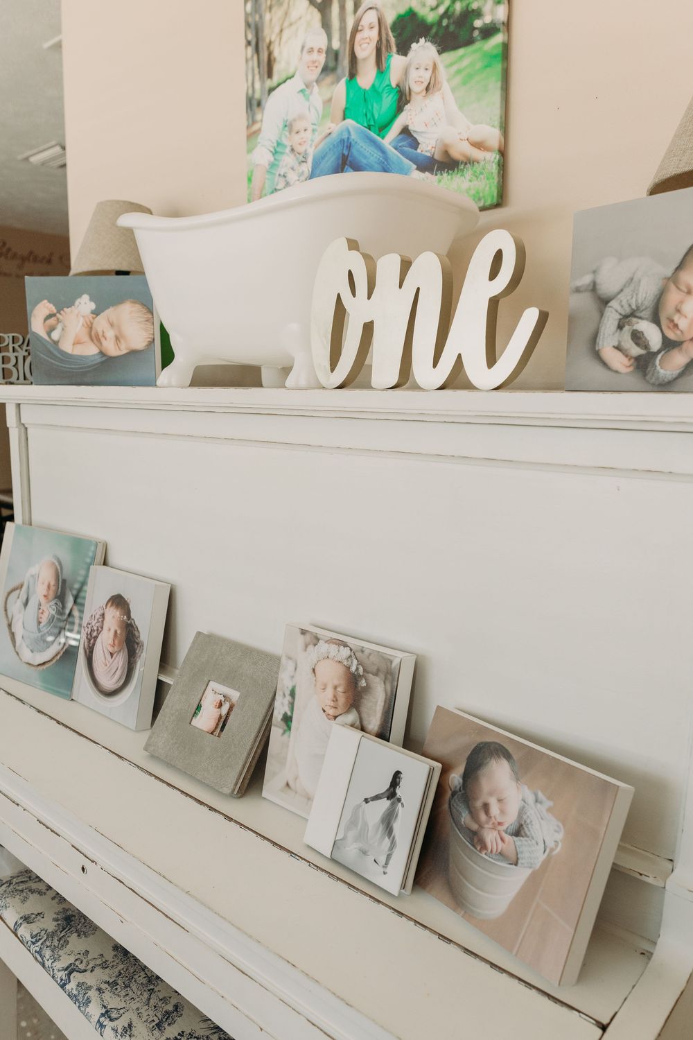 White vintage piano decorated with photo frames and a cursive 'one' sign on top, showcasing a shabby chic style.