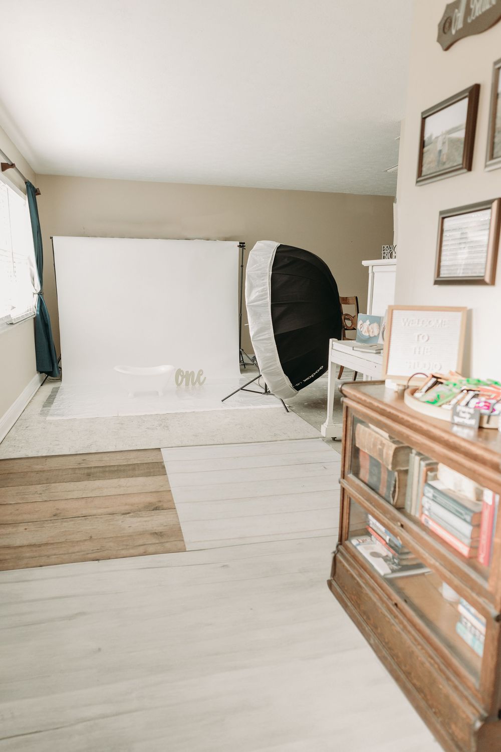 Professional photography studio setup with white backdrop, large softbox and wooden storage cabinet on light flooring.