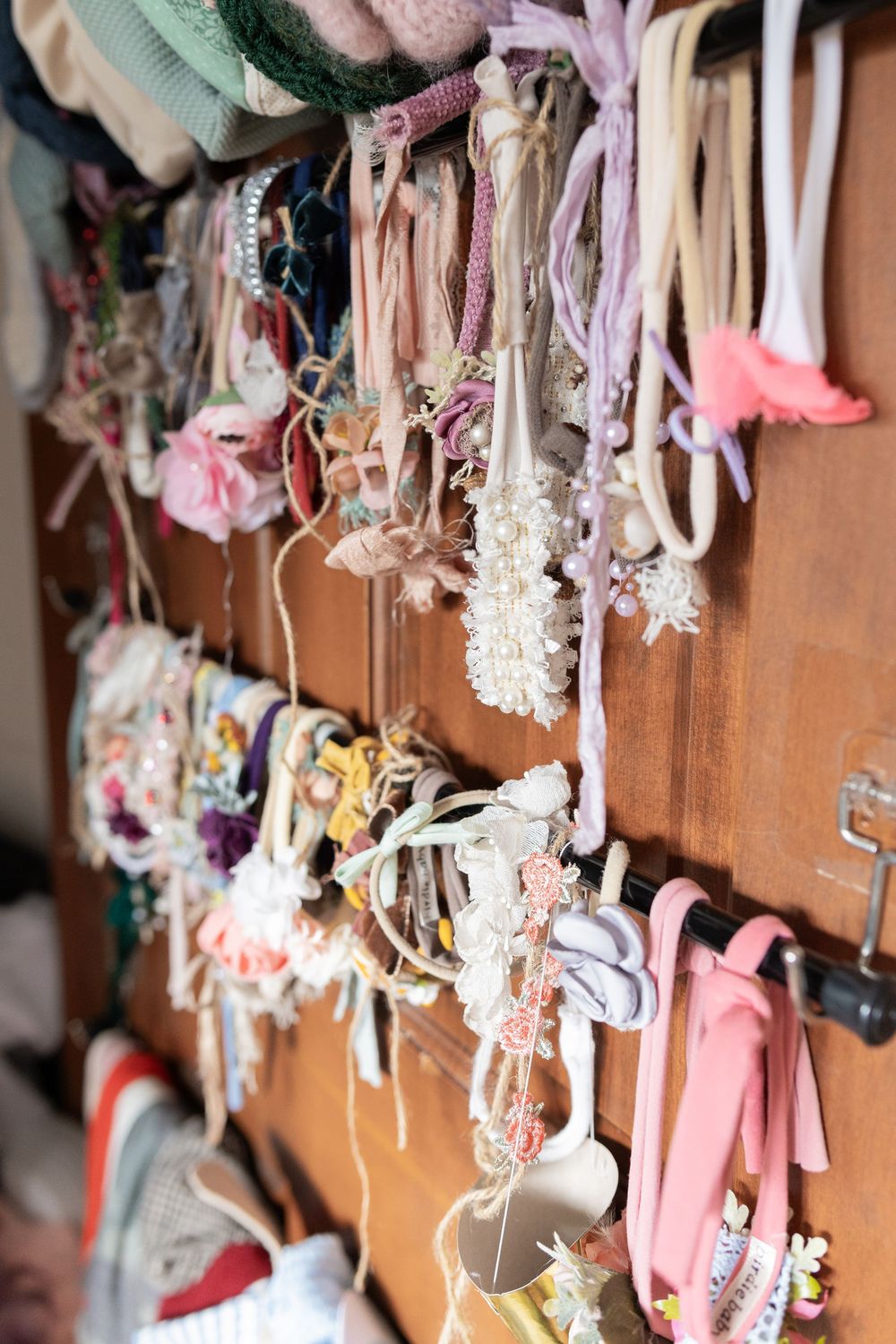 Collection of delicate pastel colored garments hanging on wooden hooks in a closet.
