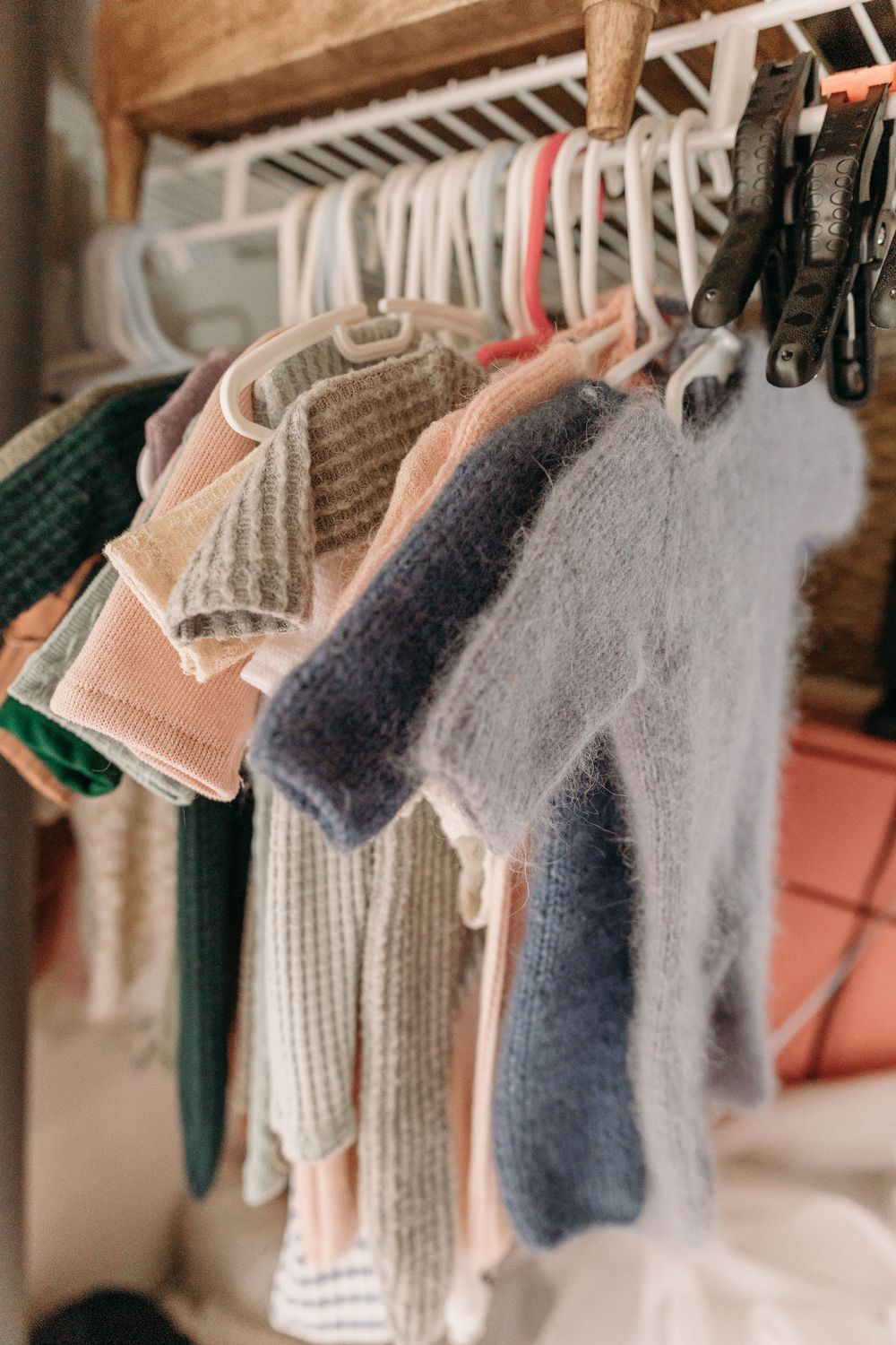 Soft knit sweaters and clothing items hanging on wooden hangers in a closet, displaying various muted colors and textures.