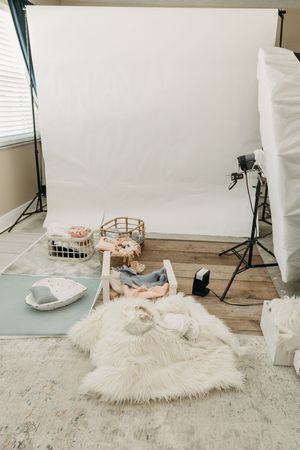 Photography studio setup with white backdrop, lighting equipment, and props scattered on wooden floor.