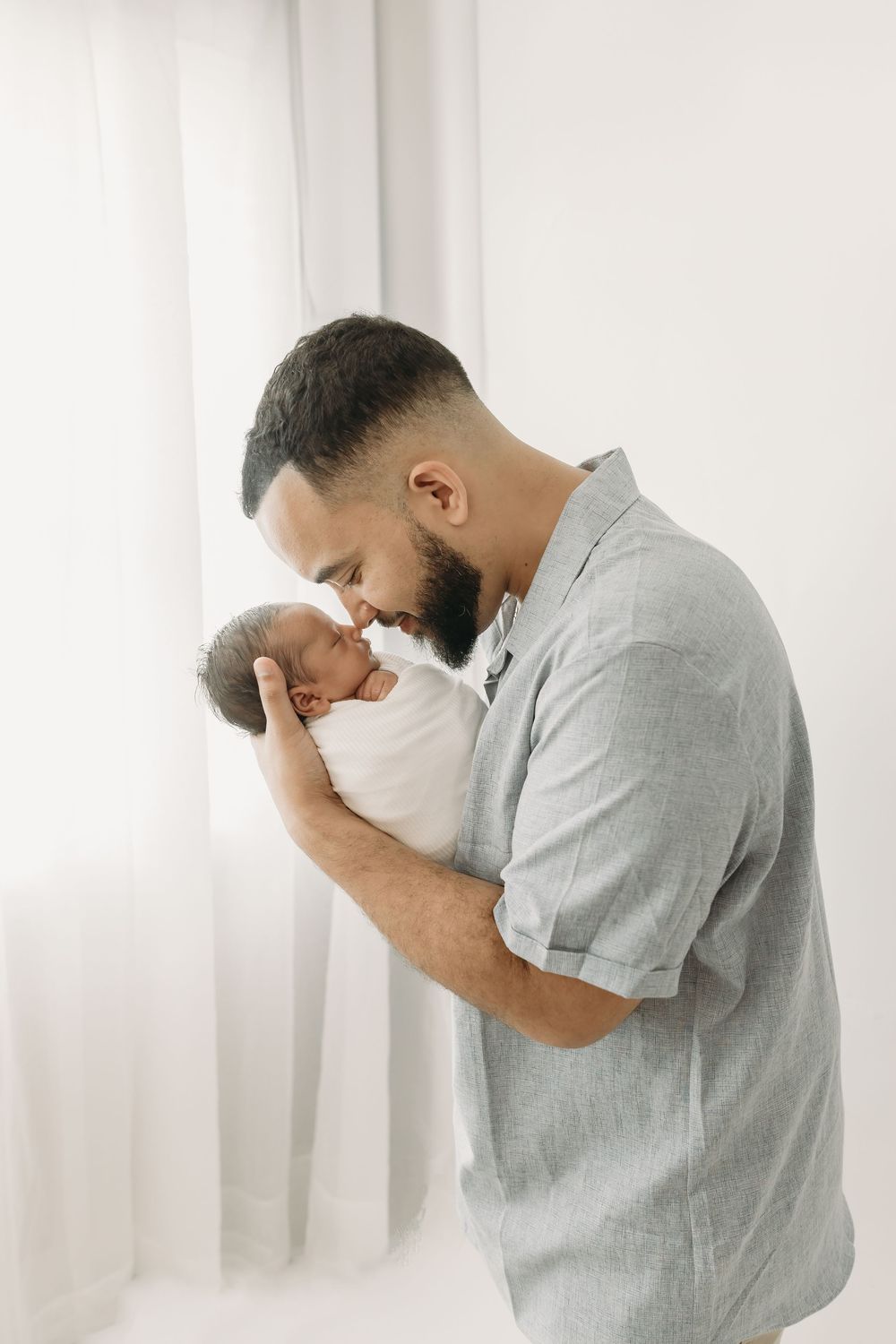 Intimate moment of parent cradling newborn baby against white curtain background.
