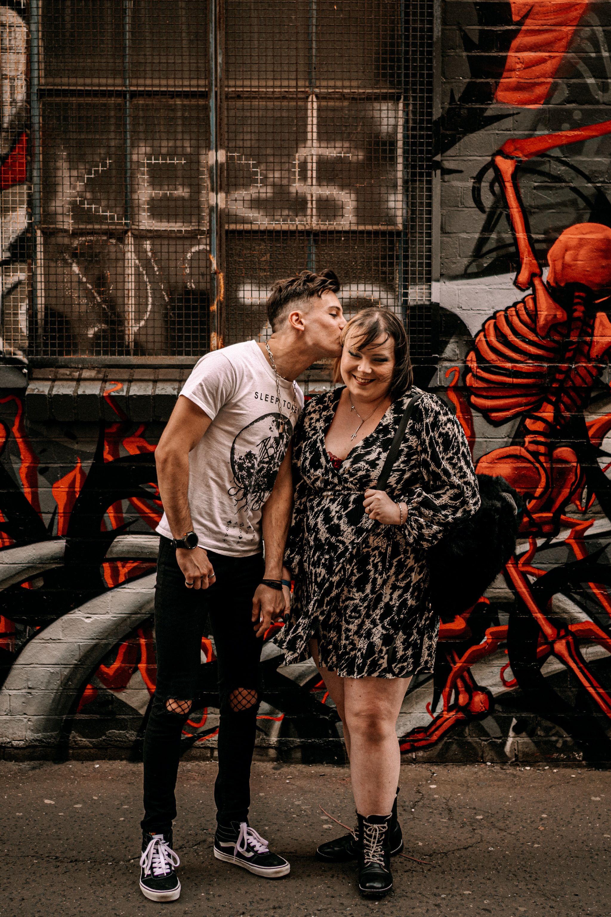 Urban couple shares tender moment against graffiti wall with colorful red artwork in industrial setting.