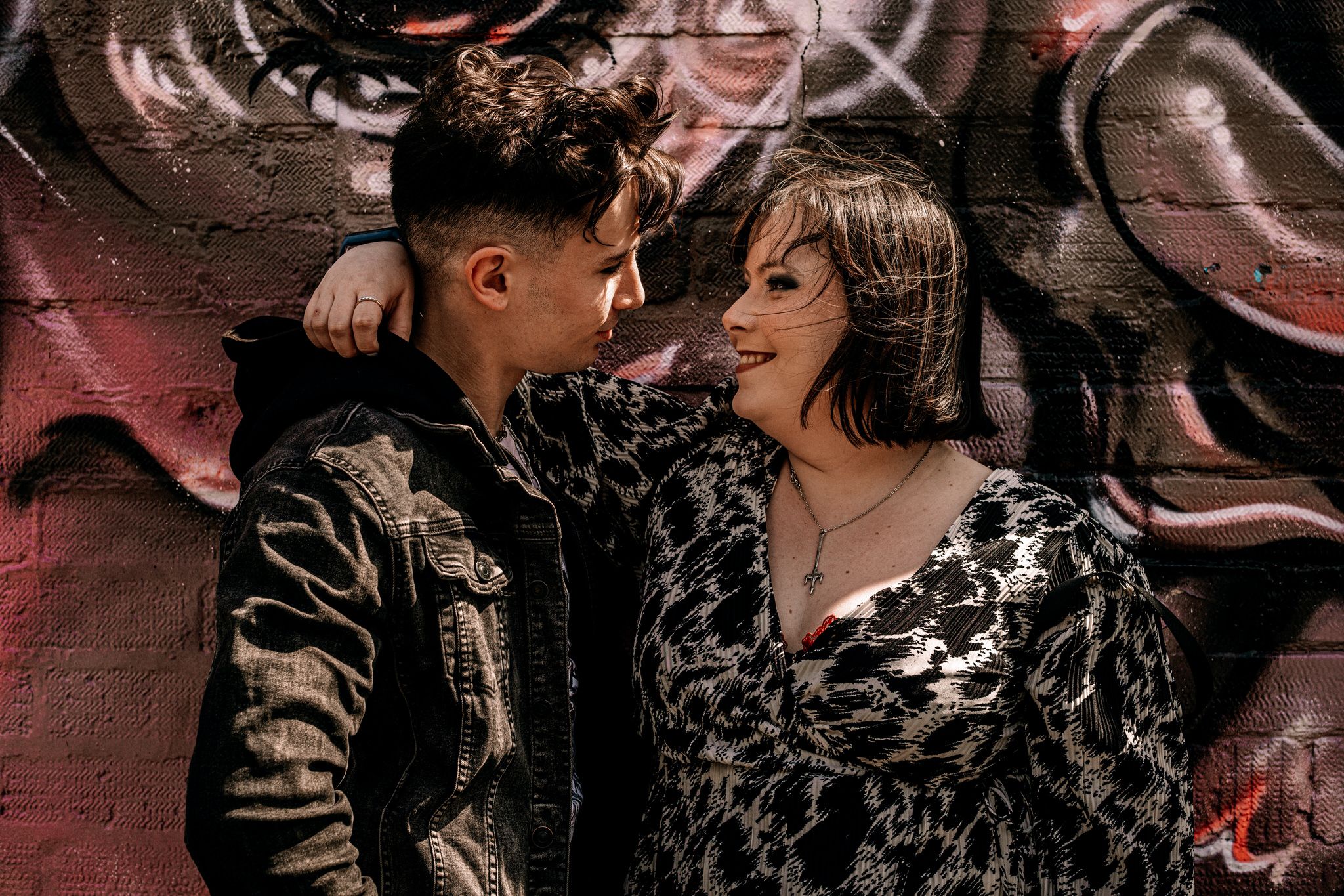 Romantic couple posing against graffiti wall with moody red lighting and urban style fashion.